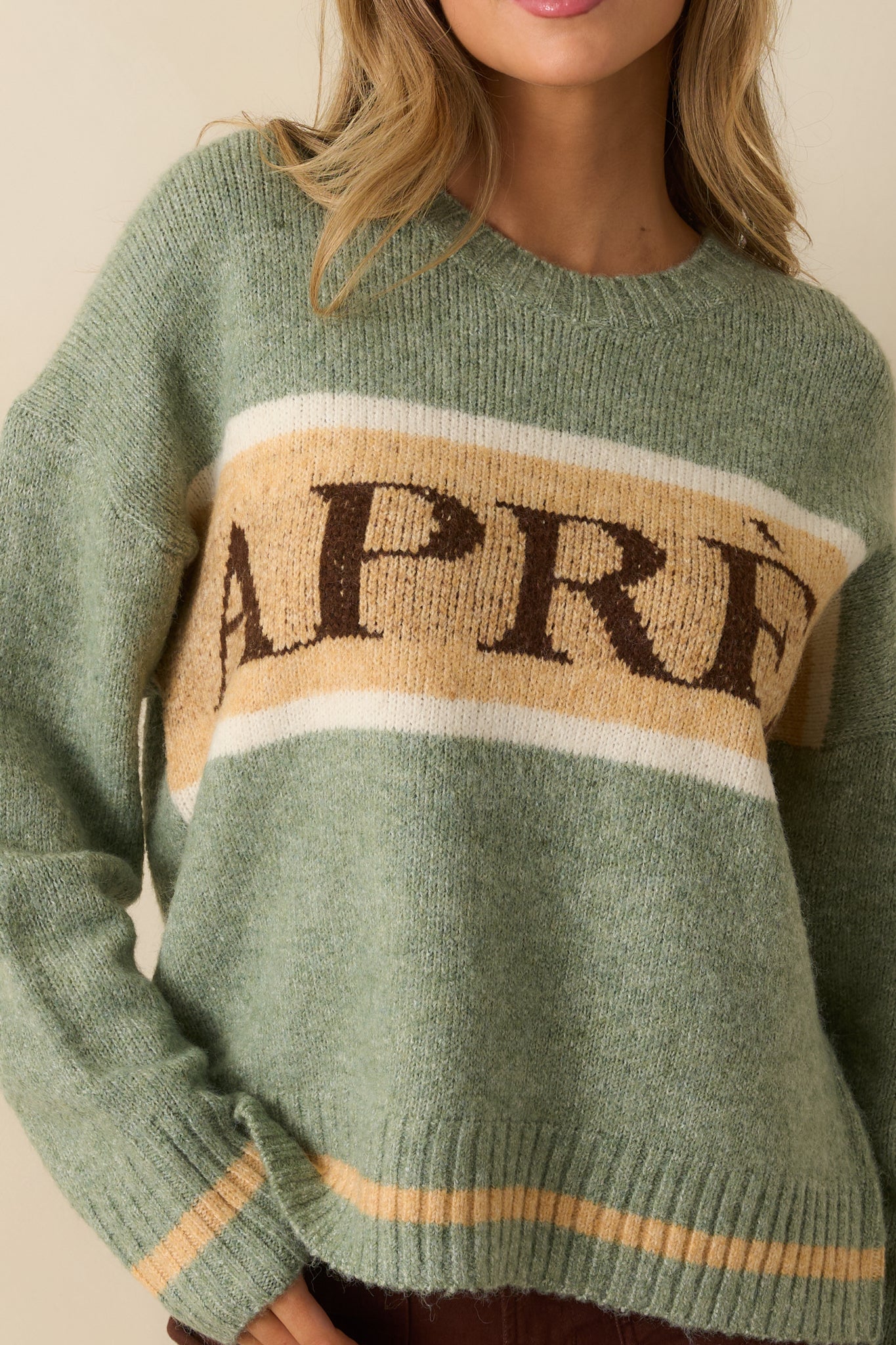 Detailed shot of the knit fabric, ribbed trim, and contrasting stripes with “APRÈS” lettering.