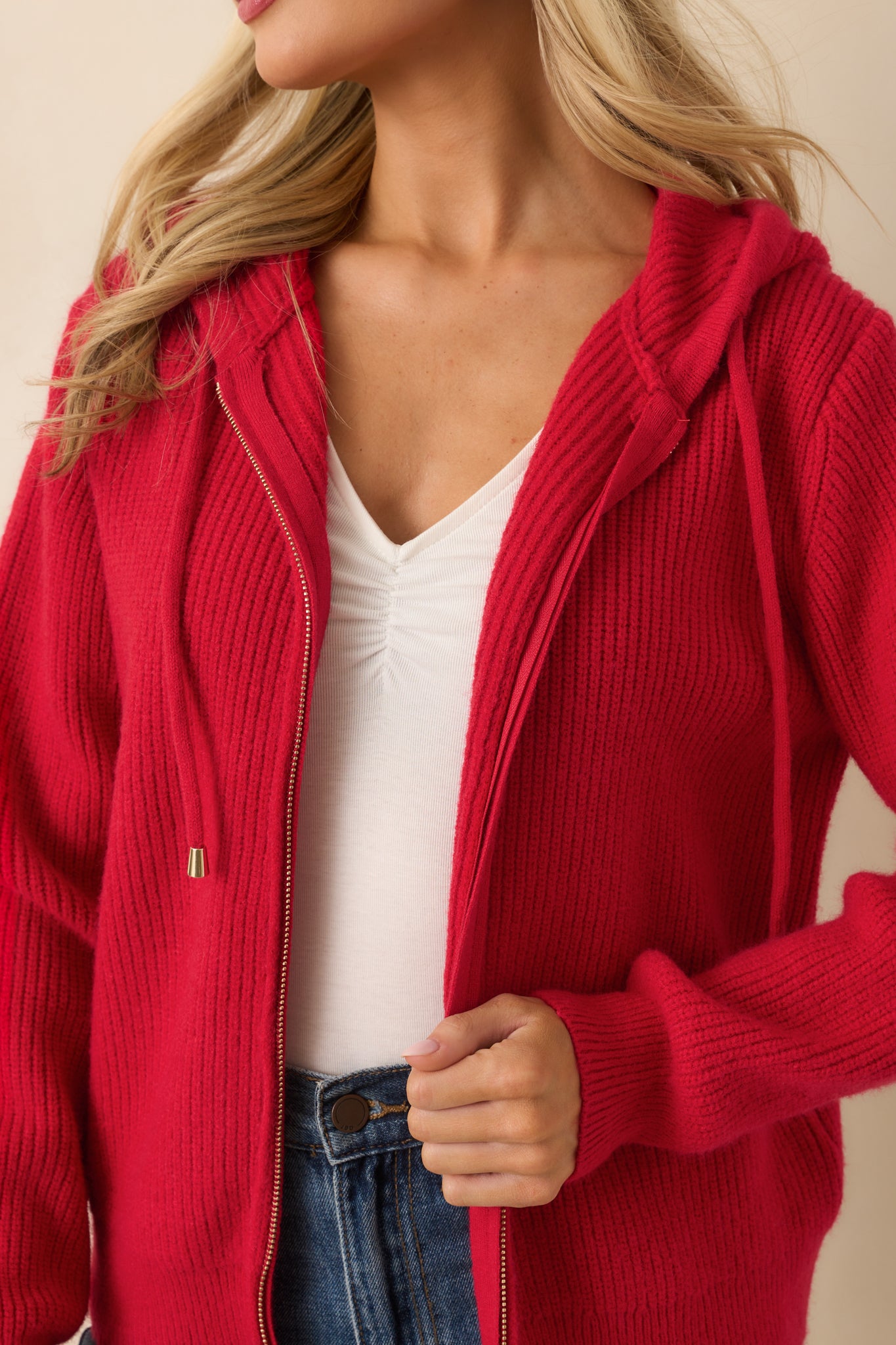 Detailed view of ribbed knit texture, zipper front, and drawstring hoodie on the red jacket.