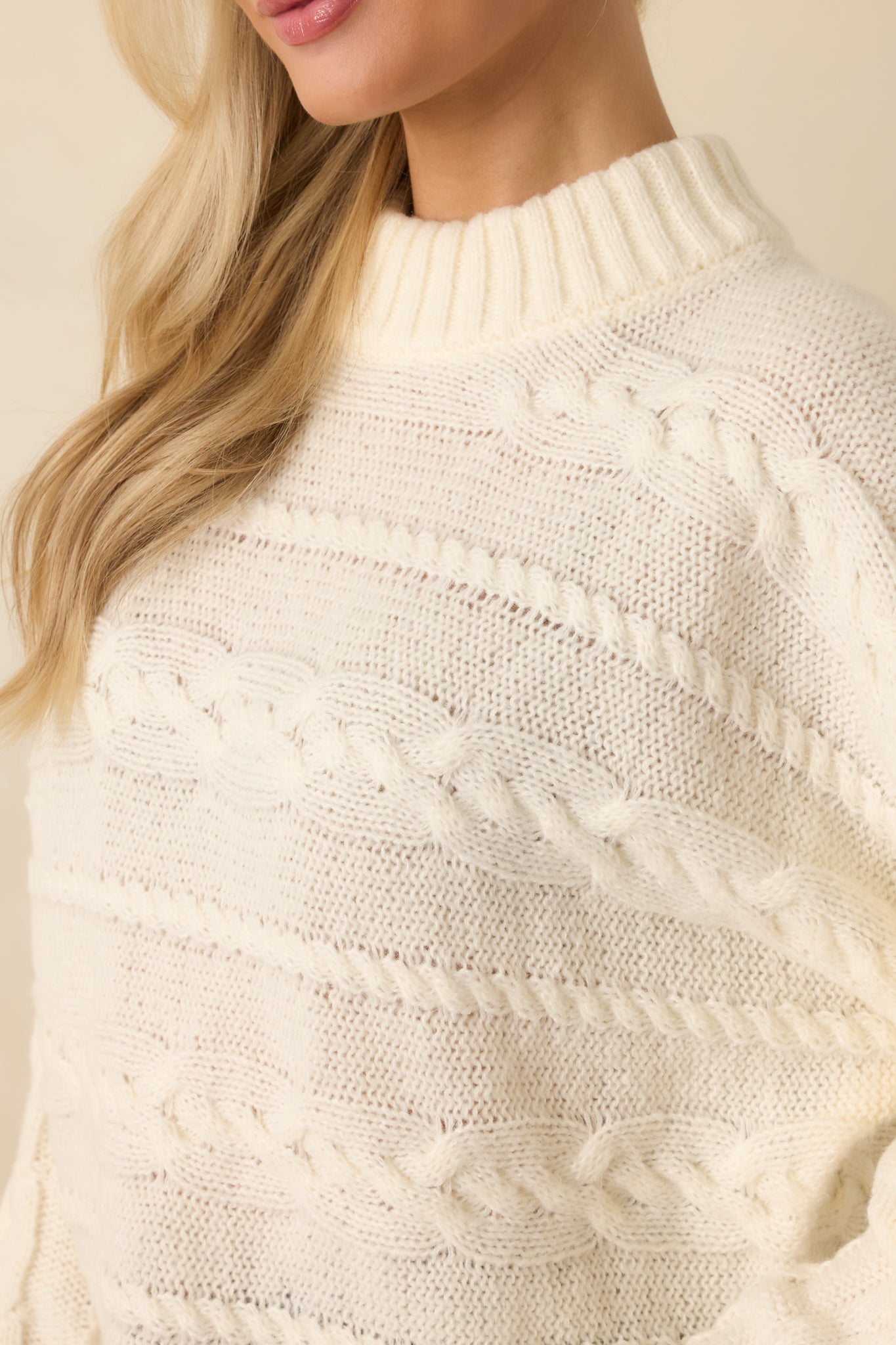 Detailed view of cable knit patterns and ribbed trim on neckline, cuffs, and hem.