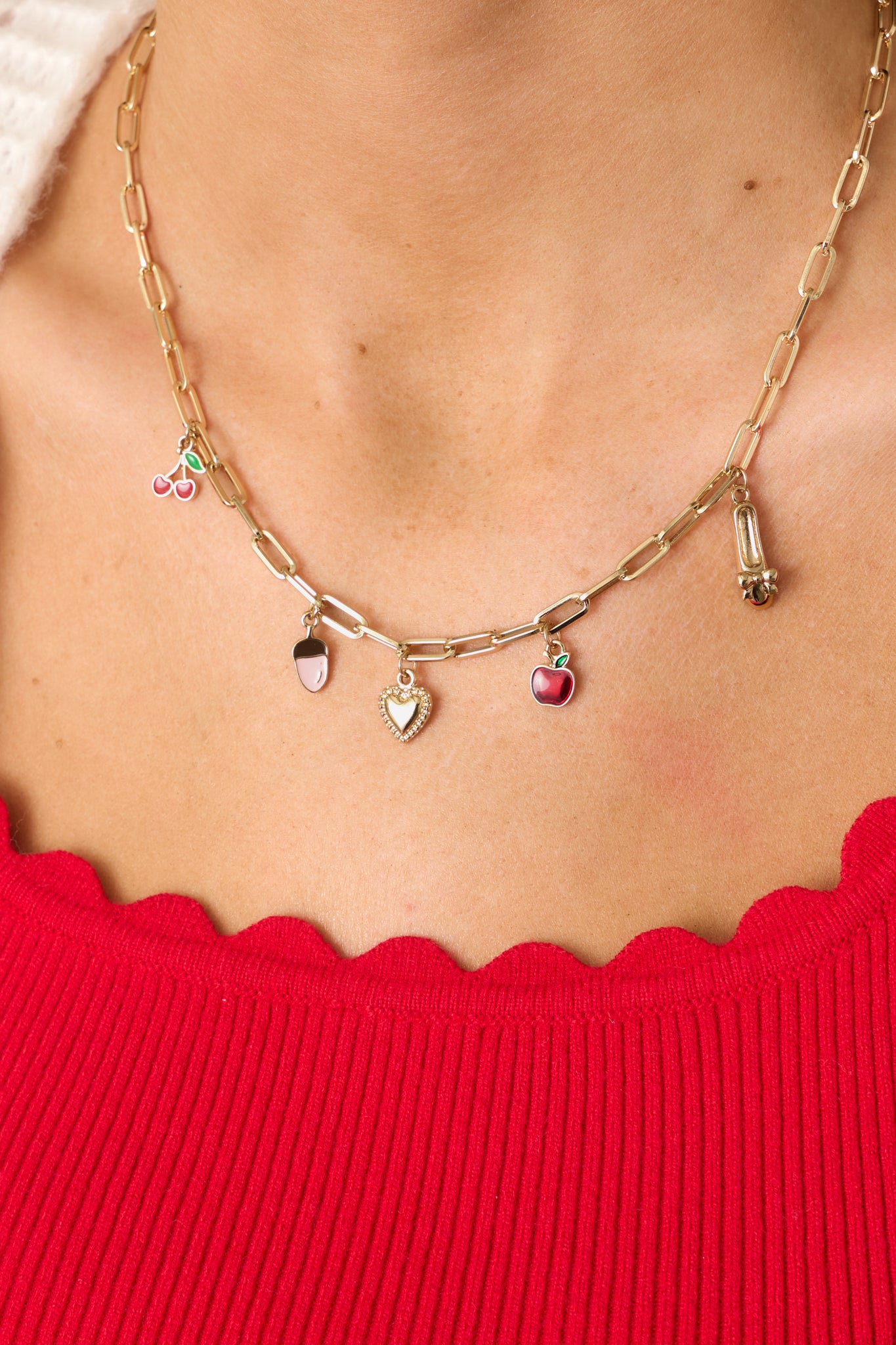 A detailed view of the necklace, highlighting the intricate gold charms, vibrant red apple and cherry accents, and polished gold hardware.