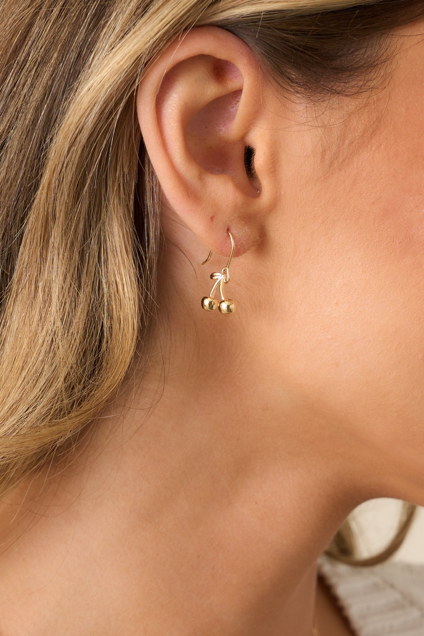 A detailed view of the gold cherry charm earrings, highlighting the intricate design, fish hook wire attachment, and clear silicone backings for a comfortable and secure wear.