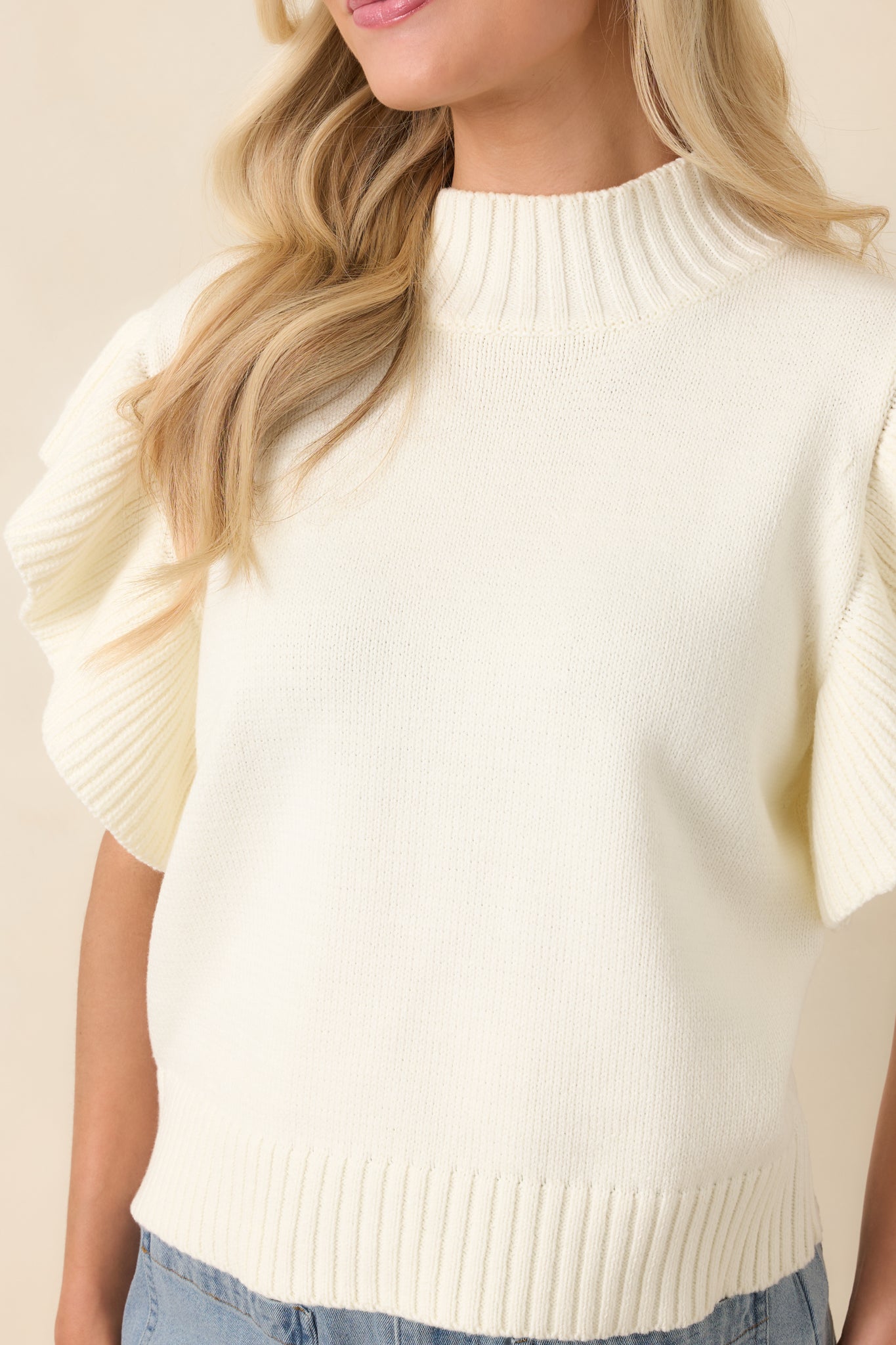 Detailed view of the ribbed mock neckline, flutter sleeve texture, and ribbed hem, highlighting the medium-weight knit construction.