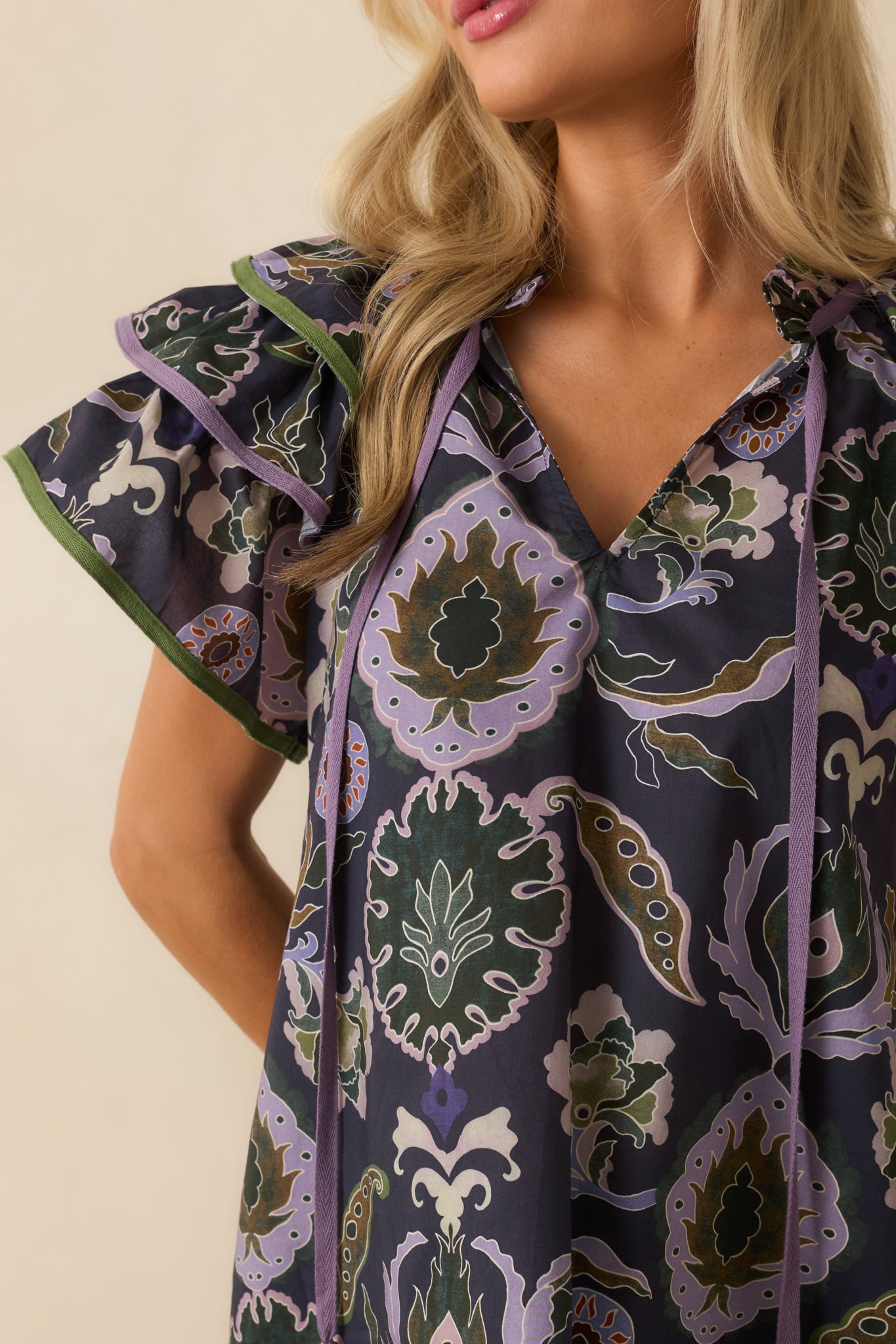 Detailed view of navy fabric with multicolor print, ruffle neckline, and self-tie tassel accents.