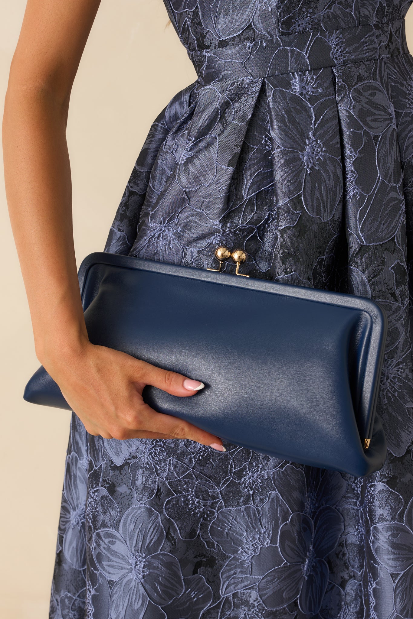 Detailed view of the gold-tone kiss-lock clasp and fine stitching on the navy faux leather clutch.