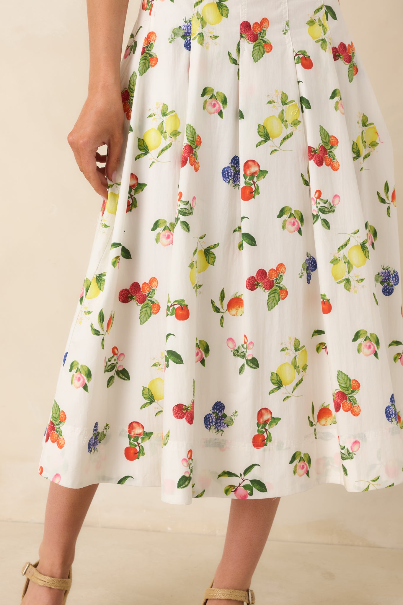 Detailed view of pleated waist and vibrant fruit pattern on white cotton midi dress