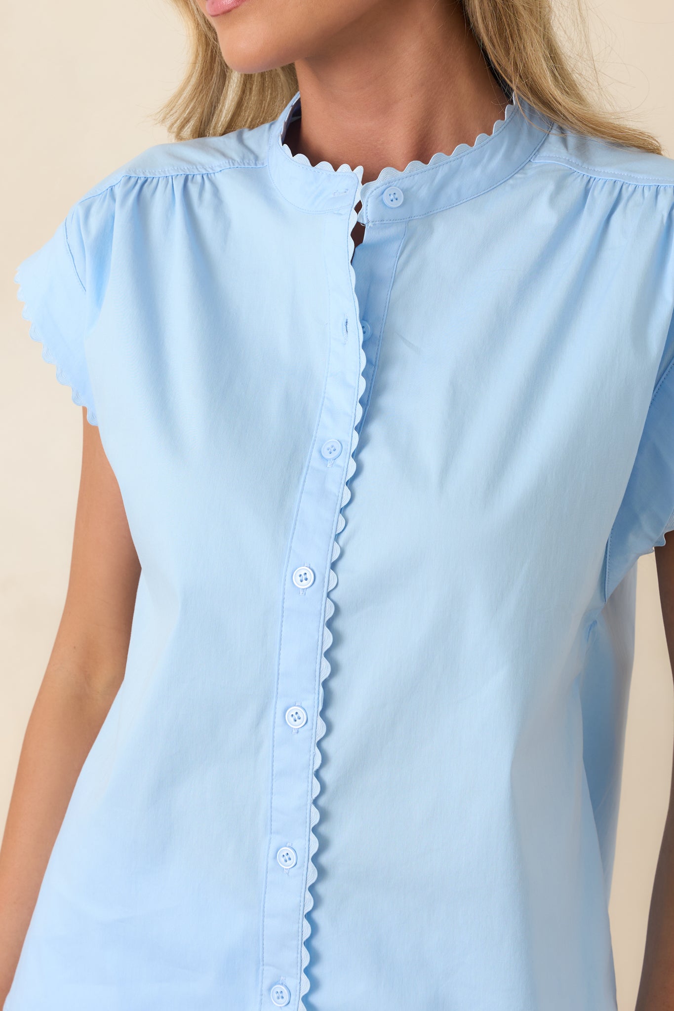 Detailed view of scalloped trim along neckline, sleeves, and button placket