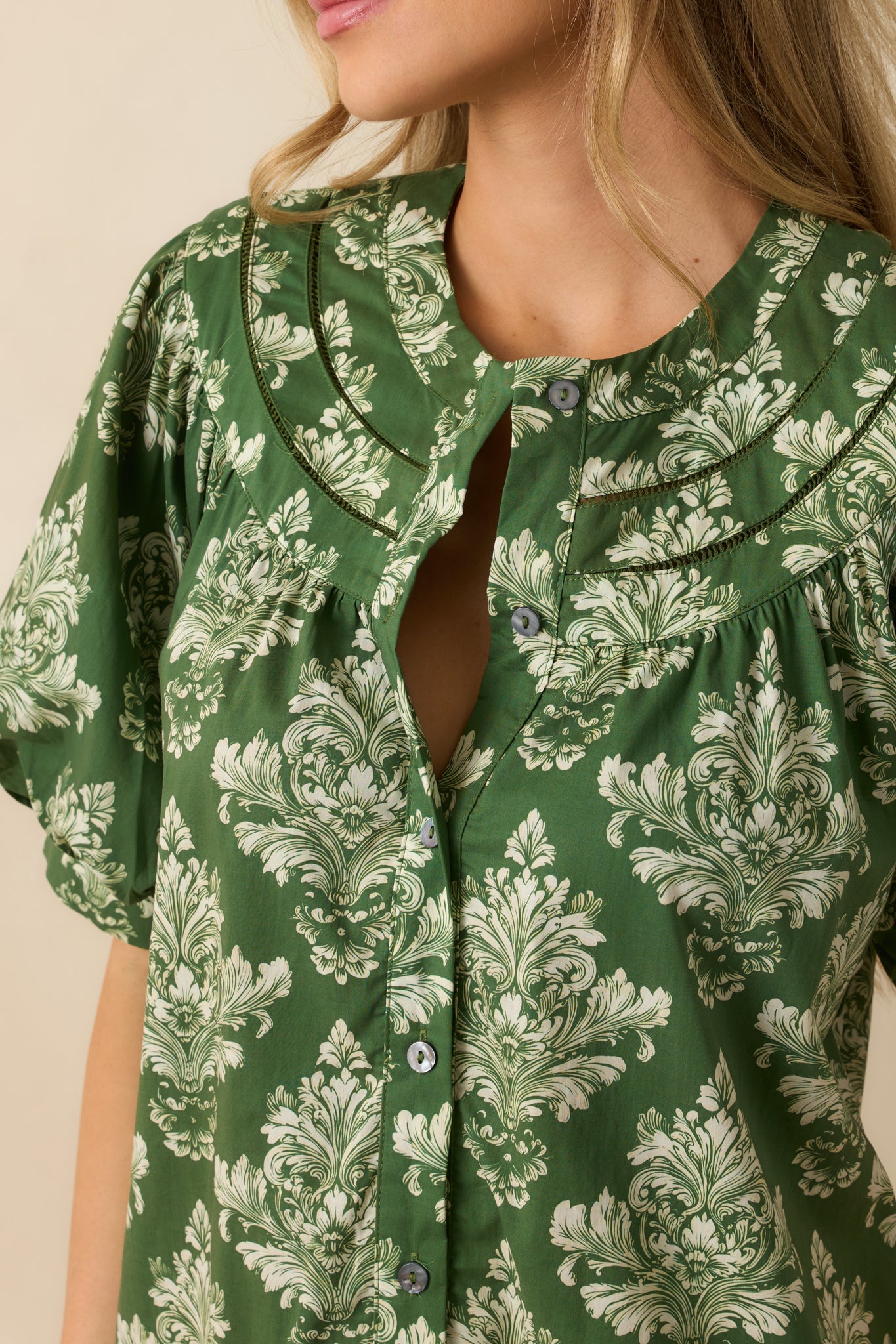 Detailed view of the green and ivory damask print, Peter Pan collar, and tiered hem of the mini dress.