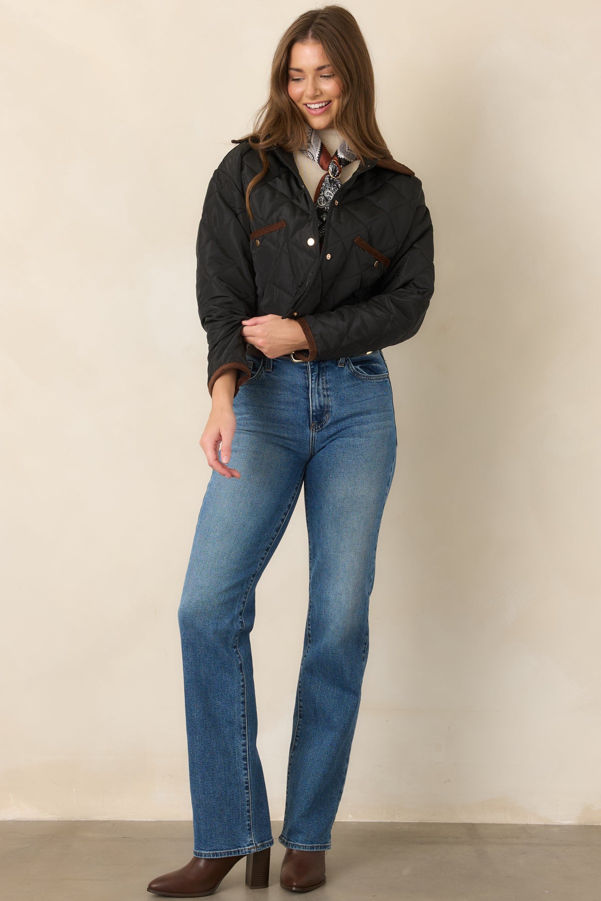 Slightly cropped diamond-stitched jacket with a brown collar, snap-front closure, and crisp black binding along the lower edges.