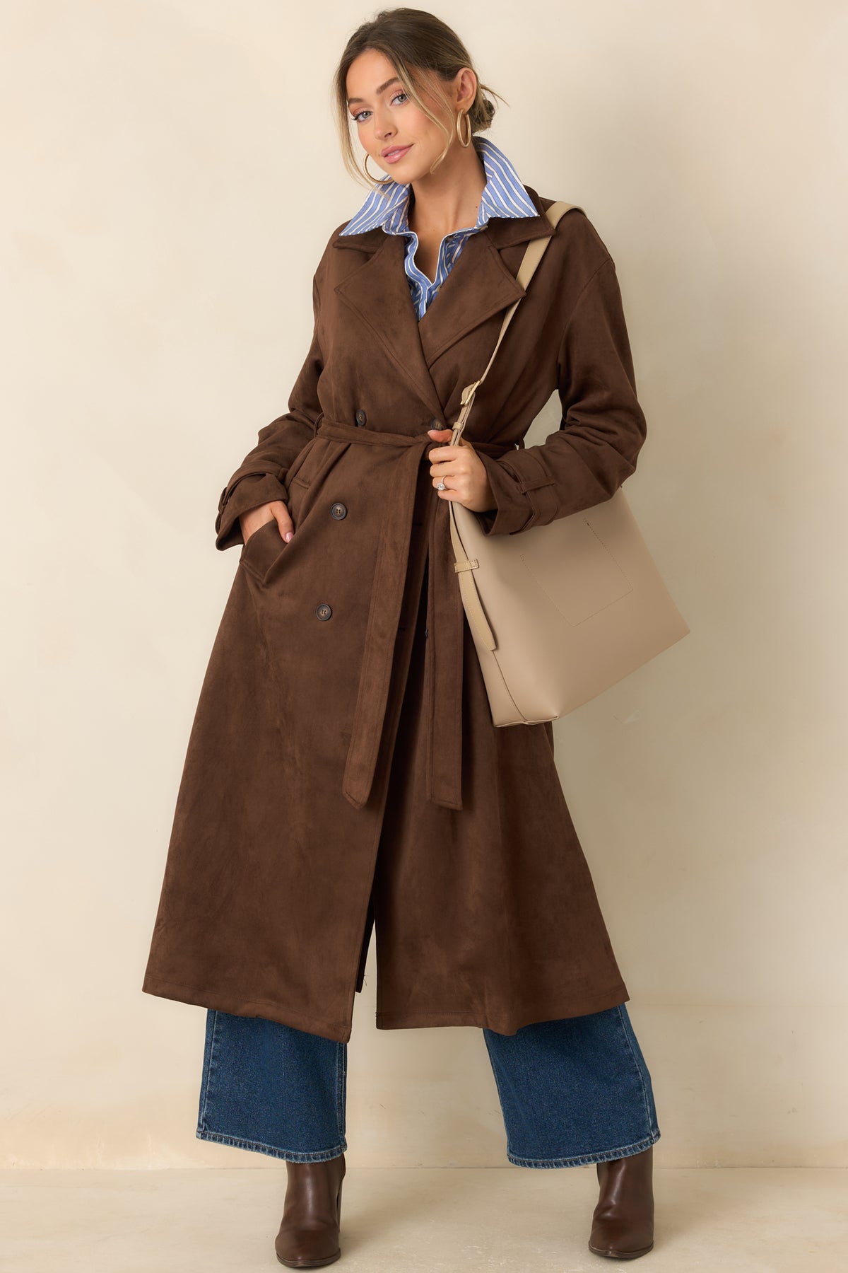 Tailored coat showcases a double-breasted front with classic buttons, a matching waist belt, and long sleeves with buttoned cuff tabs.