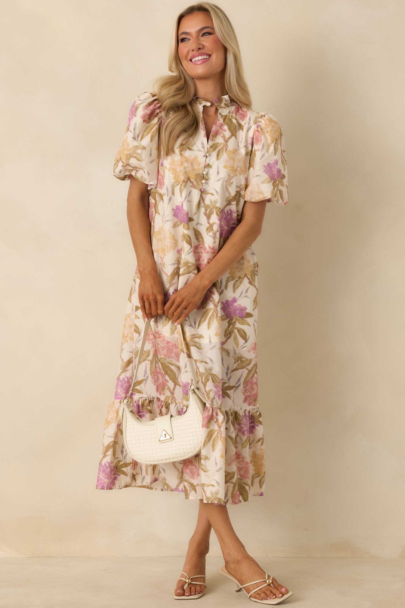 Soft ivory midi dress showcasing an allover muted floral print, puff sleeves, and a delicate ruffled collar. The partial button-front detail and flowing ruffle hem create an easy, feminine silhouette.