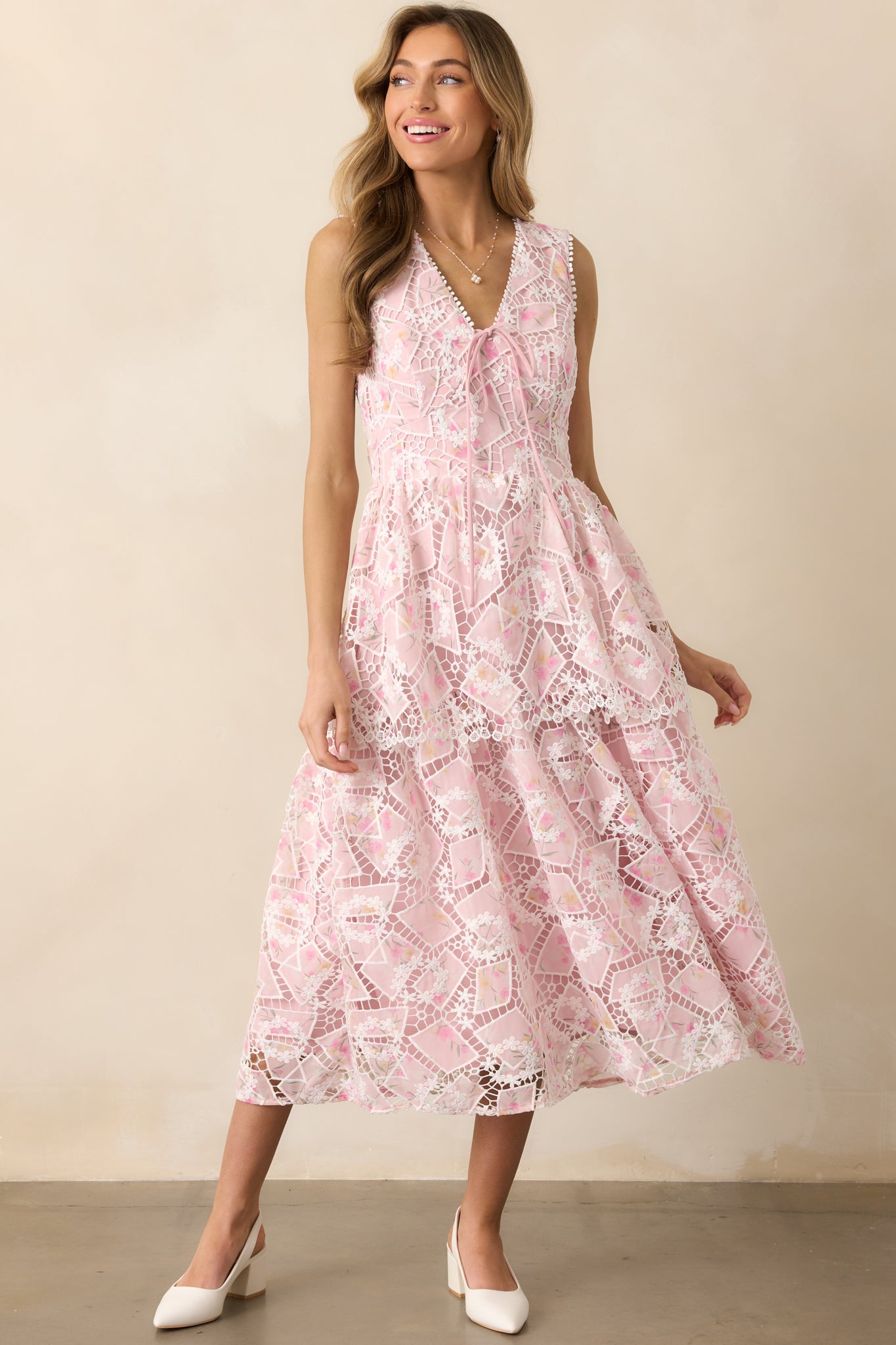 A romantic dress with a white floral tulle overlay, a soft pink lining, adjustable straps, and a tiered skirt for an elegant flow.