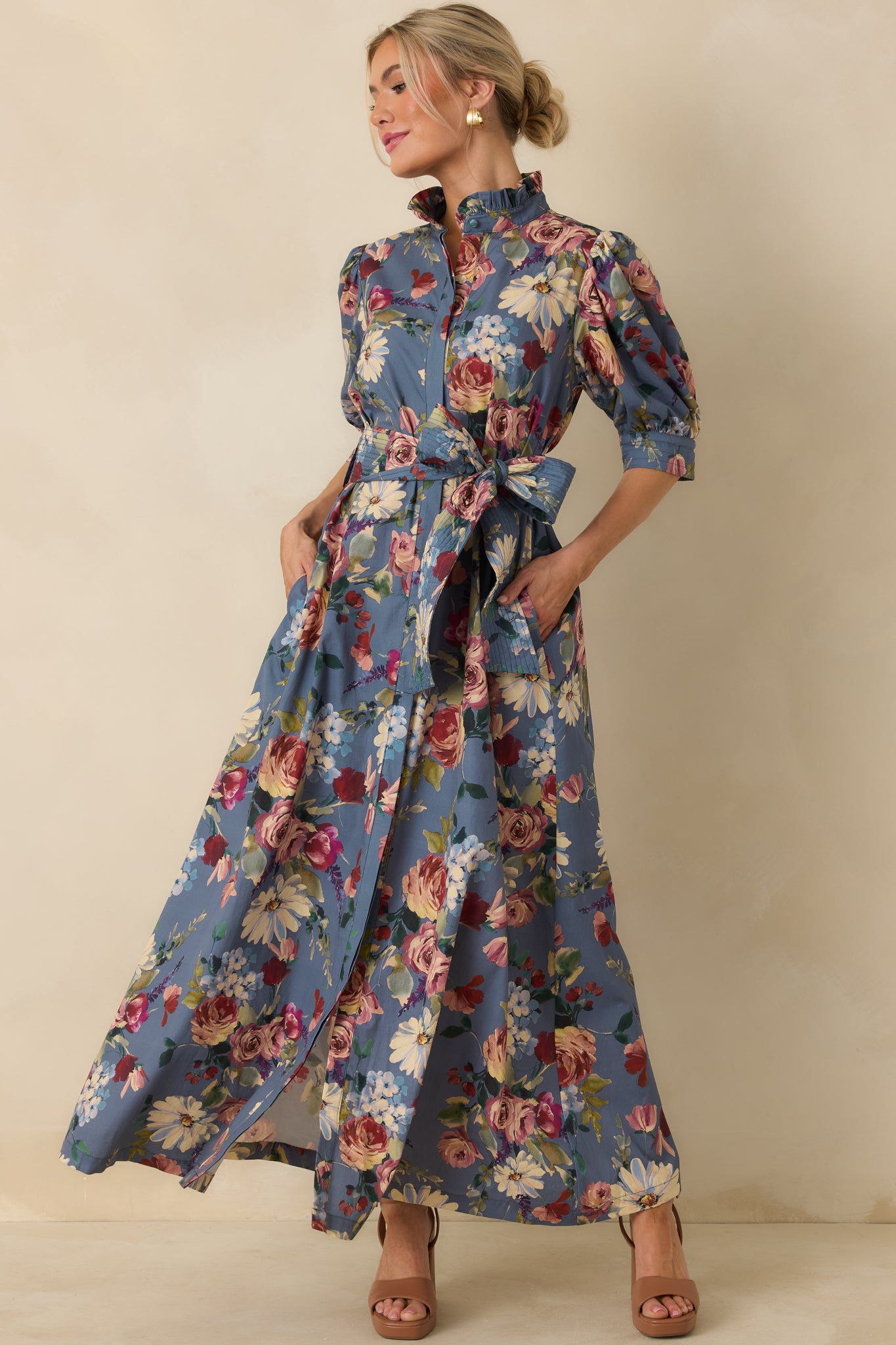 Dusty blue cotton maxi dress featuring abundant floral blooms, a ruffled stand collar, and puffed elbow-length sleeves.