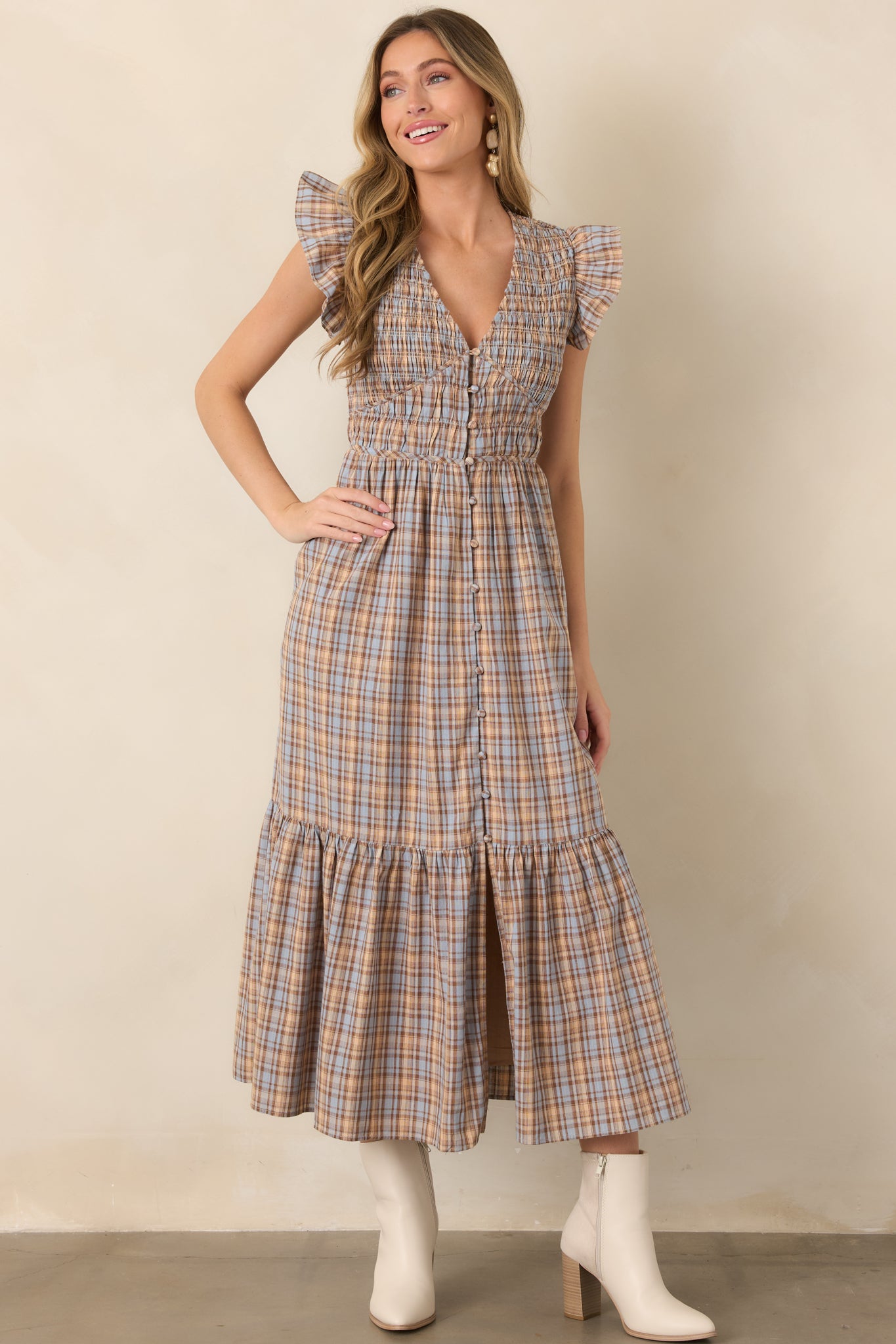 Dusty blue plaid dress accented with warm tan and brown tones, featuring a smocked bodice, flutter sleeves, and tiered midi skirt.