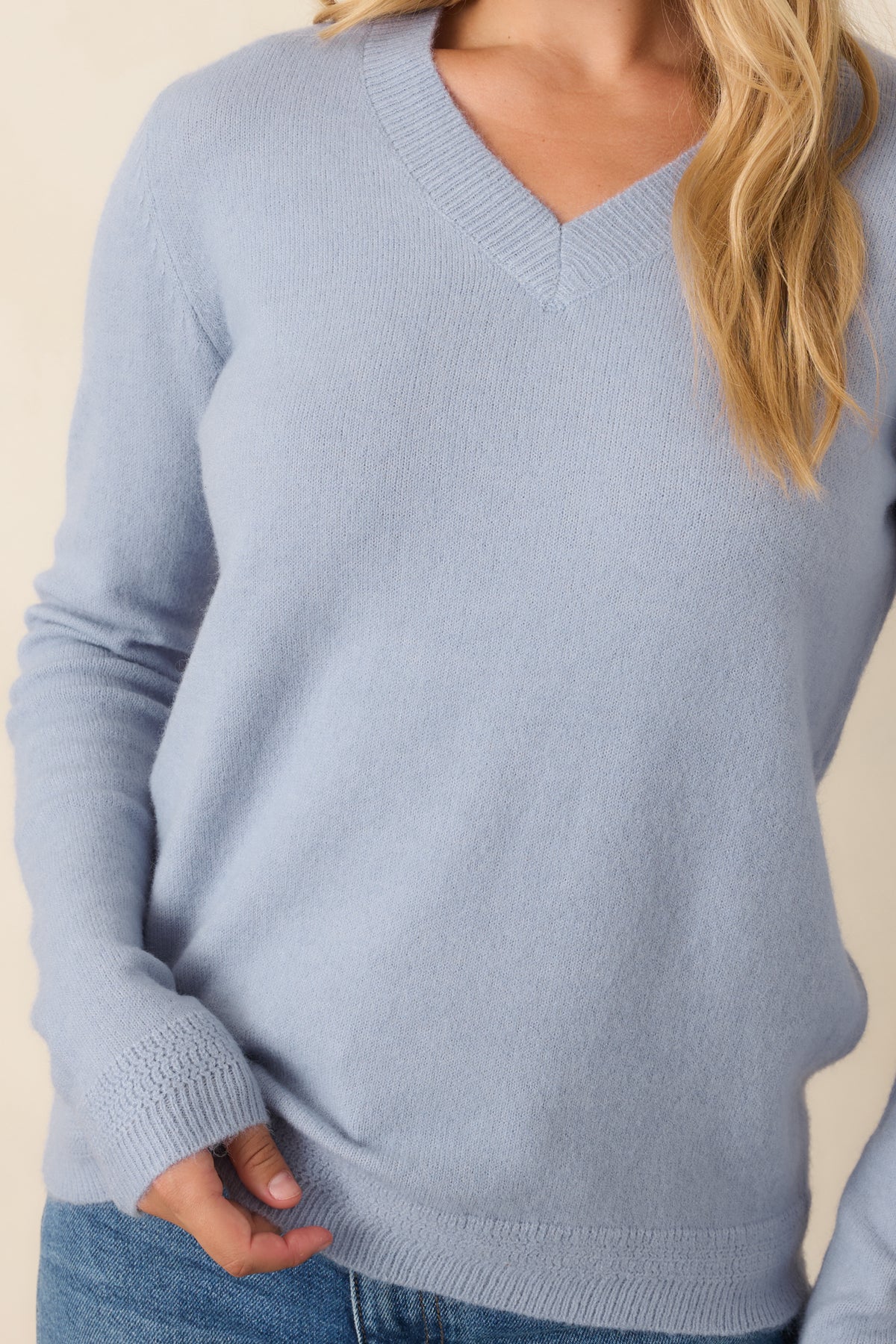 Close-up detail of the dusty blue knit top highlighting the V-neckline, soft sweater texture, and ribbed trim.