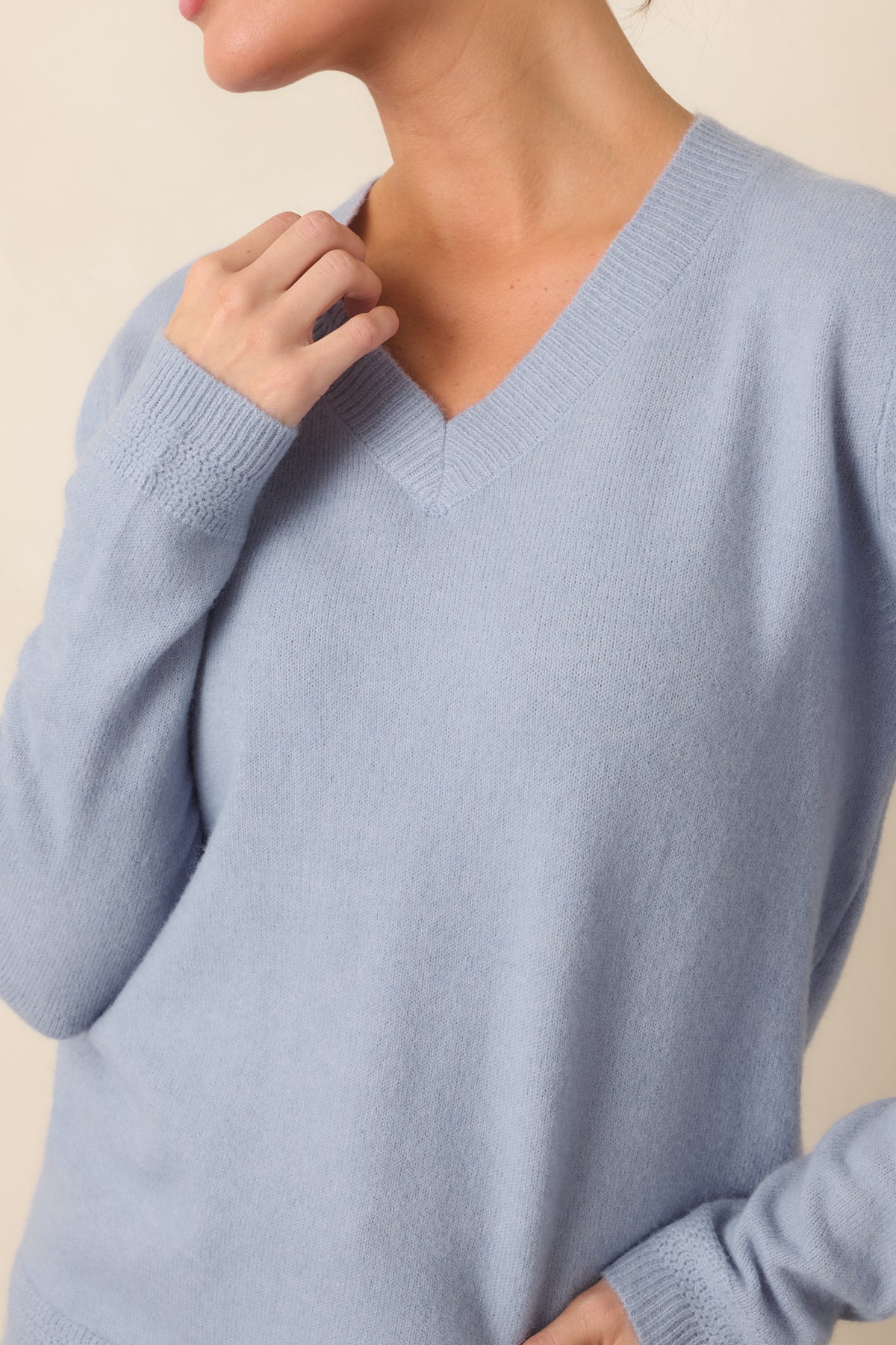 Close-up detail highlighting the V-neckline and ribbed trim of the dusty blue knit.