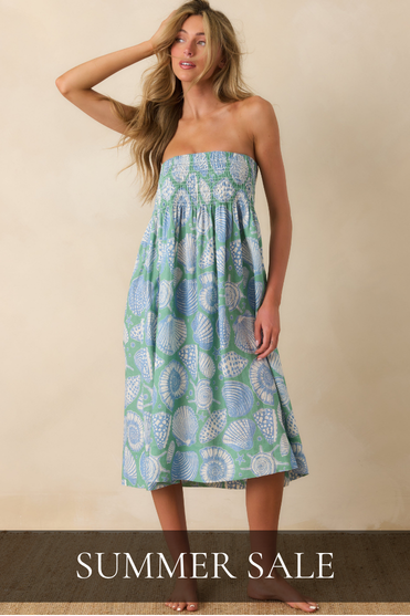 Woman in a sea foam green and light blue, shell print, strapless dress against a beige background. 