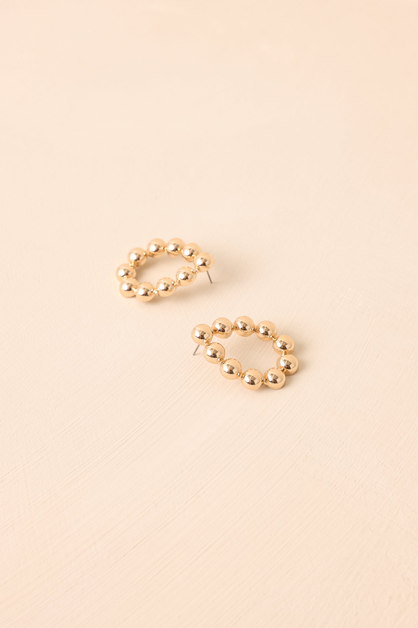 Flat lay of the earrings on a beige surface emphasizing the teardrop silhouette and uniform beaded detailing.