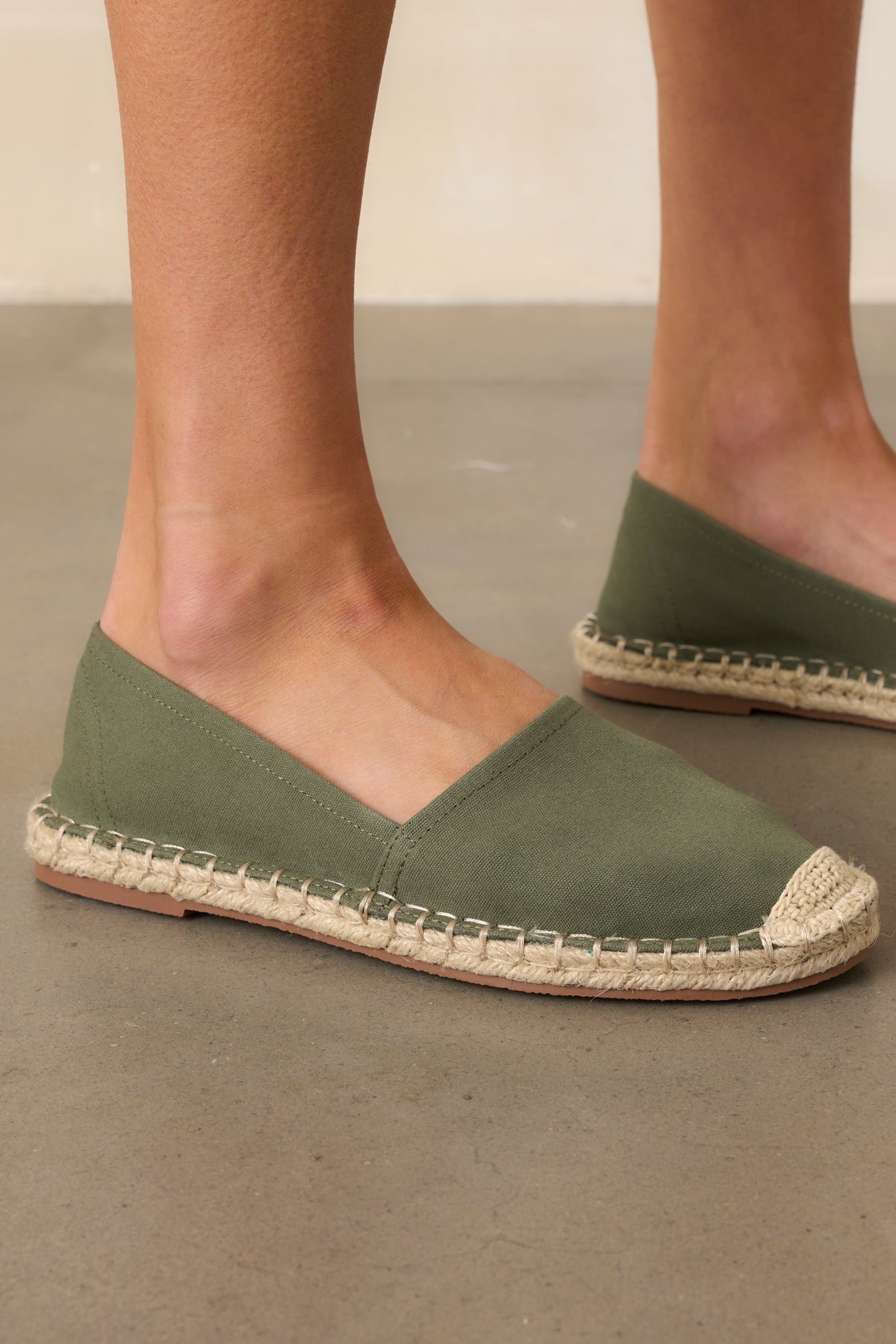 Earthy green flat shoes displayed at a side angle, featuring canvas fabric and espadrille jute soles.