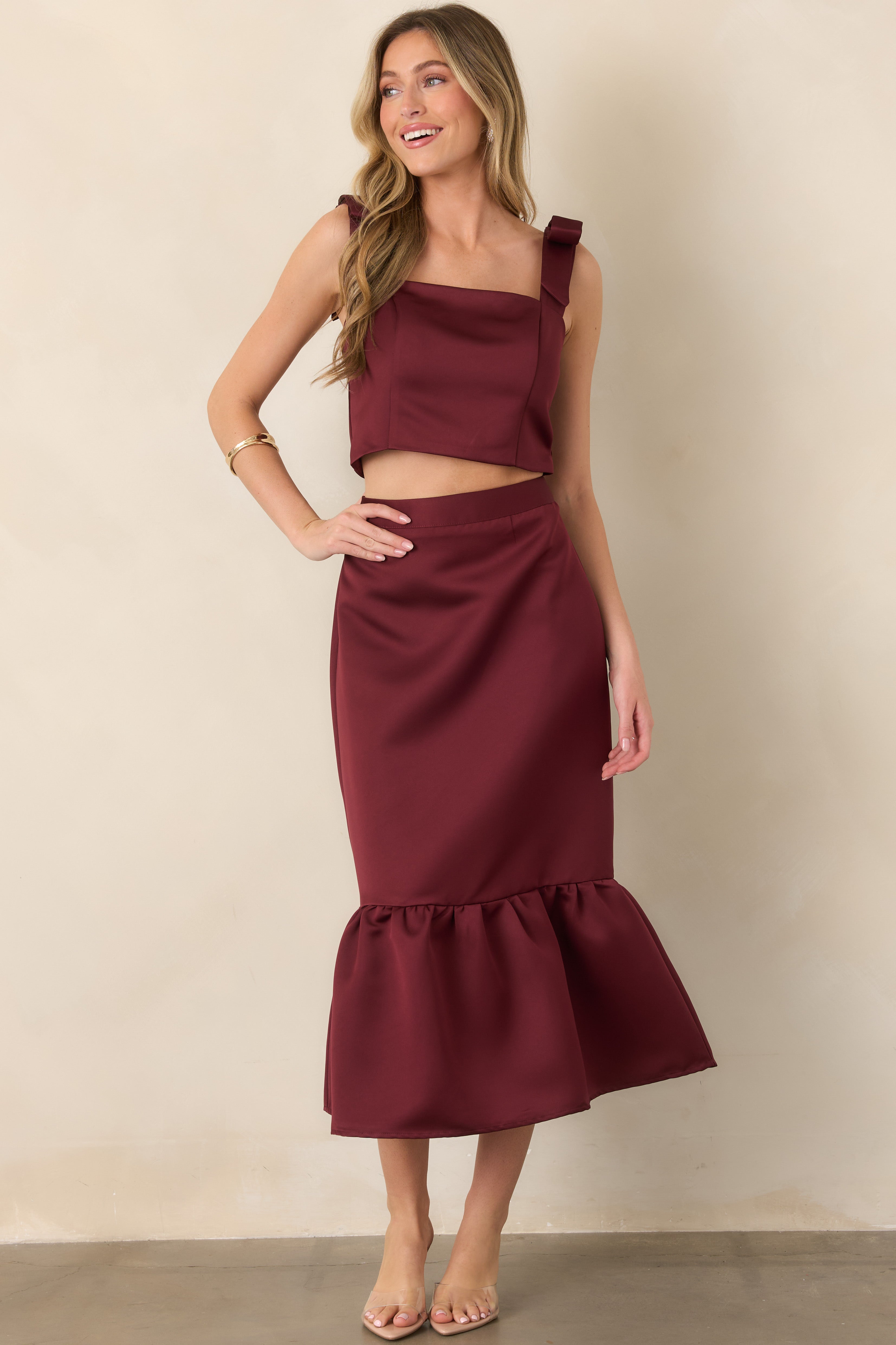Elegant satin skirt highlighting its streamlined midi silhouette, glossy burgundy fabric, and graceful flounced hem with gathered detailing.