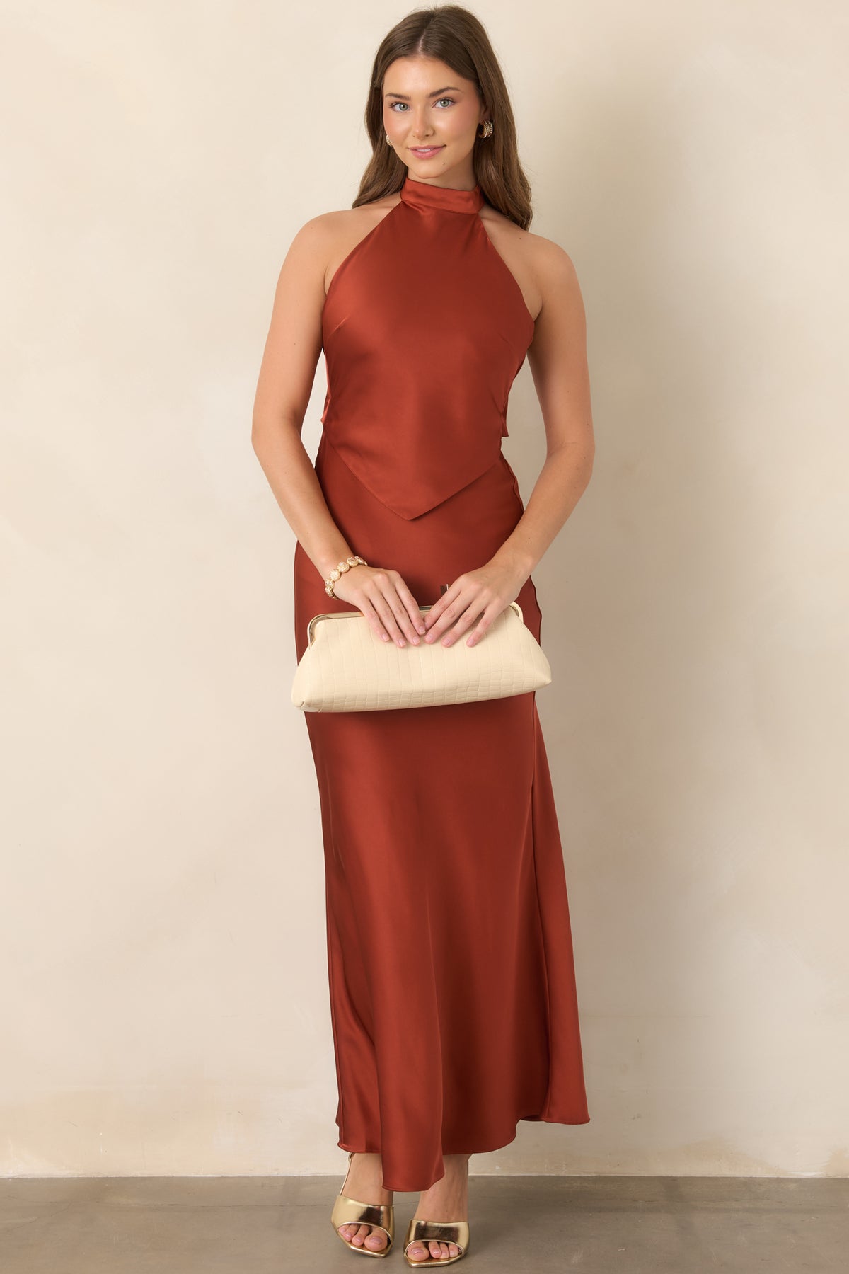 Elegant burnt sienna satin dress with a sleek halter neckline, pointed bodice overlay, and softly flowing maxi-length skirt.