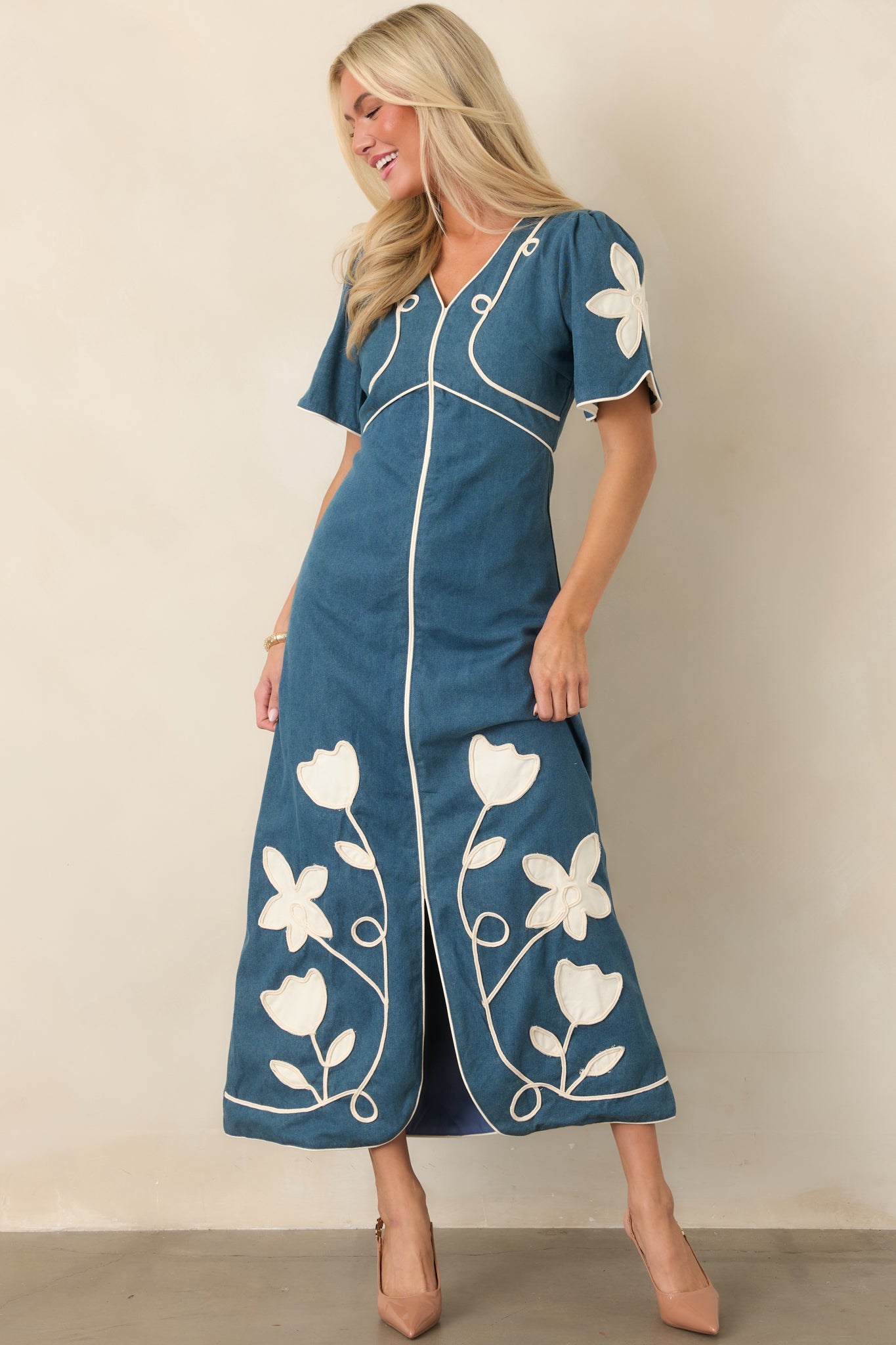 Elegant maxi silhouette featuring decorative floral appliqué, contrast piping, a defined waist, and softly flared skirt.