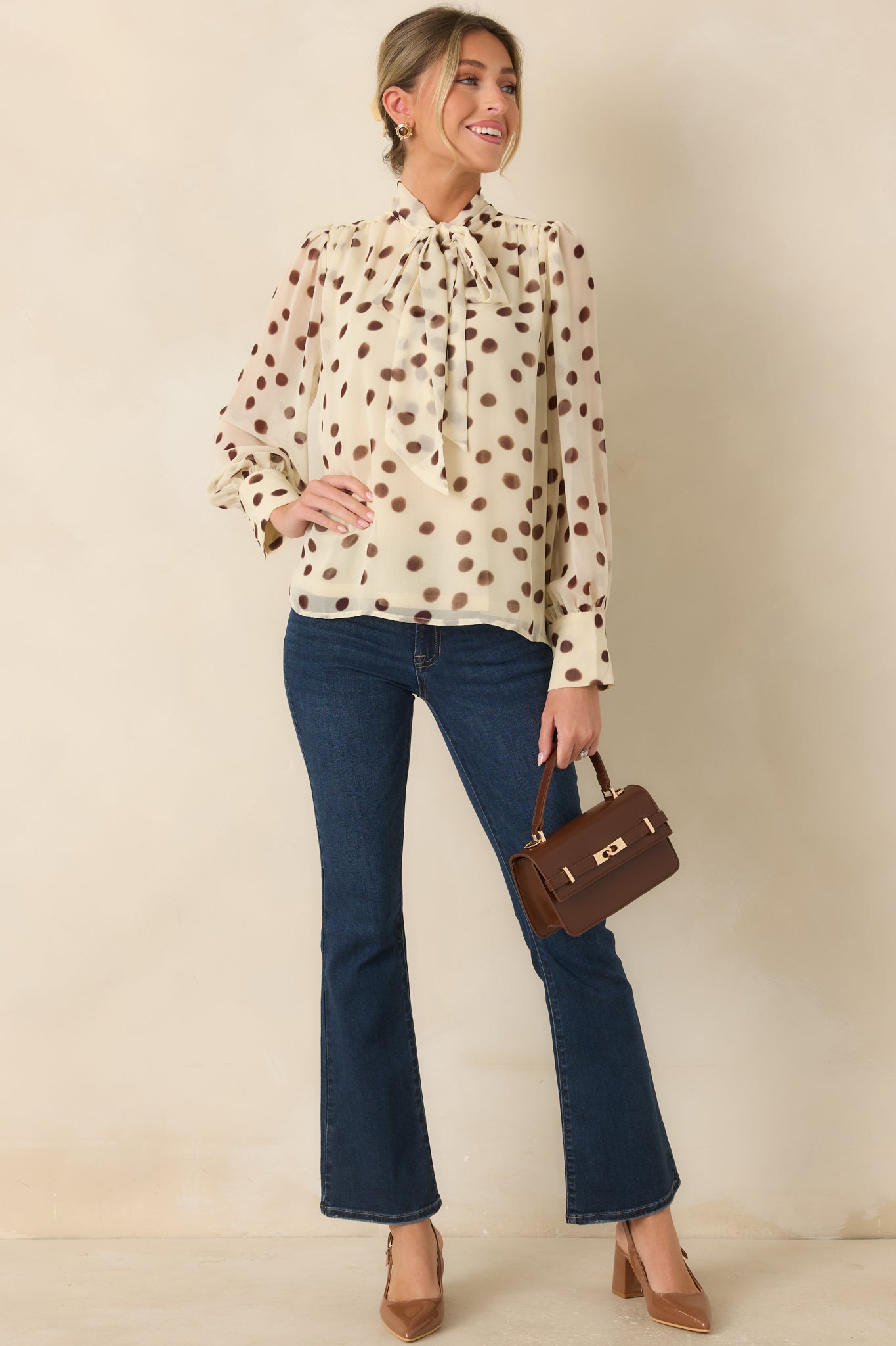 Elegant ivory blouse showcasing a graceful self-tie neckline, long sleeves, button cuffs, and delicate brown dot pattern.