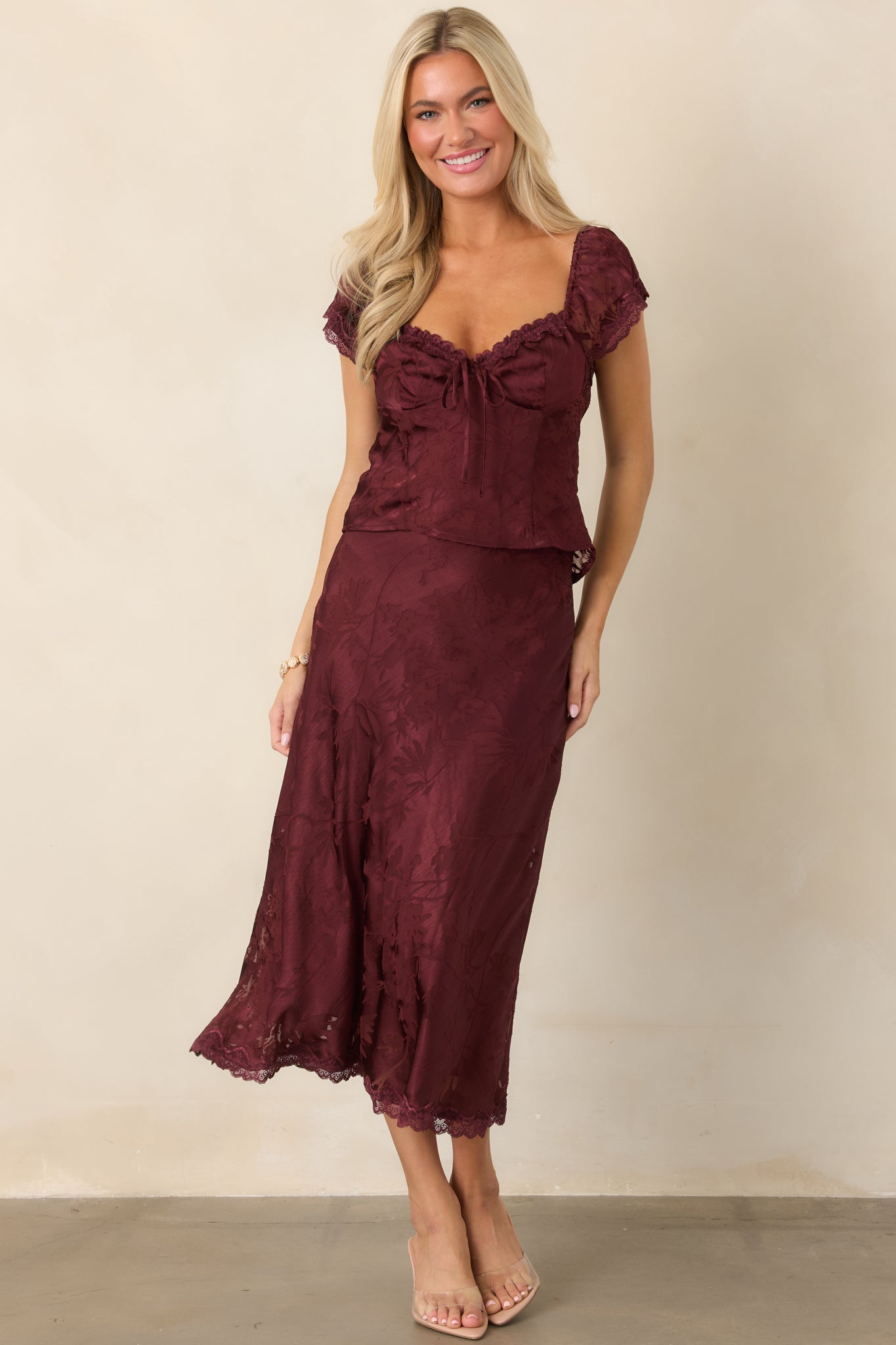 Elegant fitted top with a tonal floral burnout pattern, delicate lace-framed neckline, adjustable front tie, and softly gathered cap sleeves.