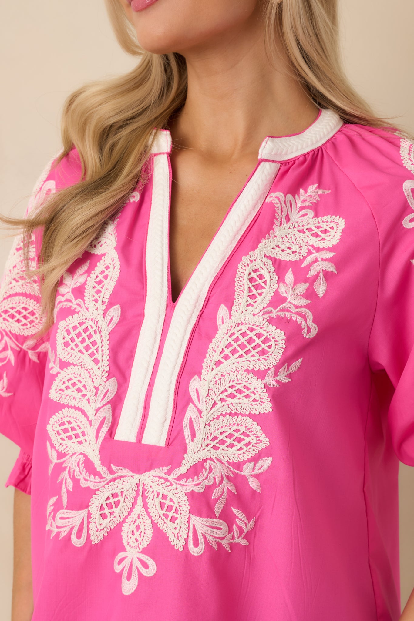 Close-up of the embroidered detailing and contrast trim on the pink V-neck top.