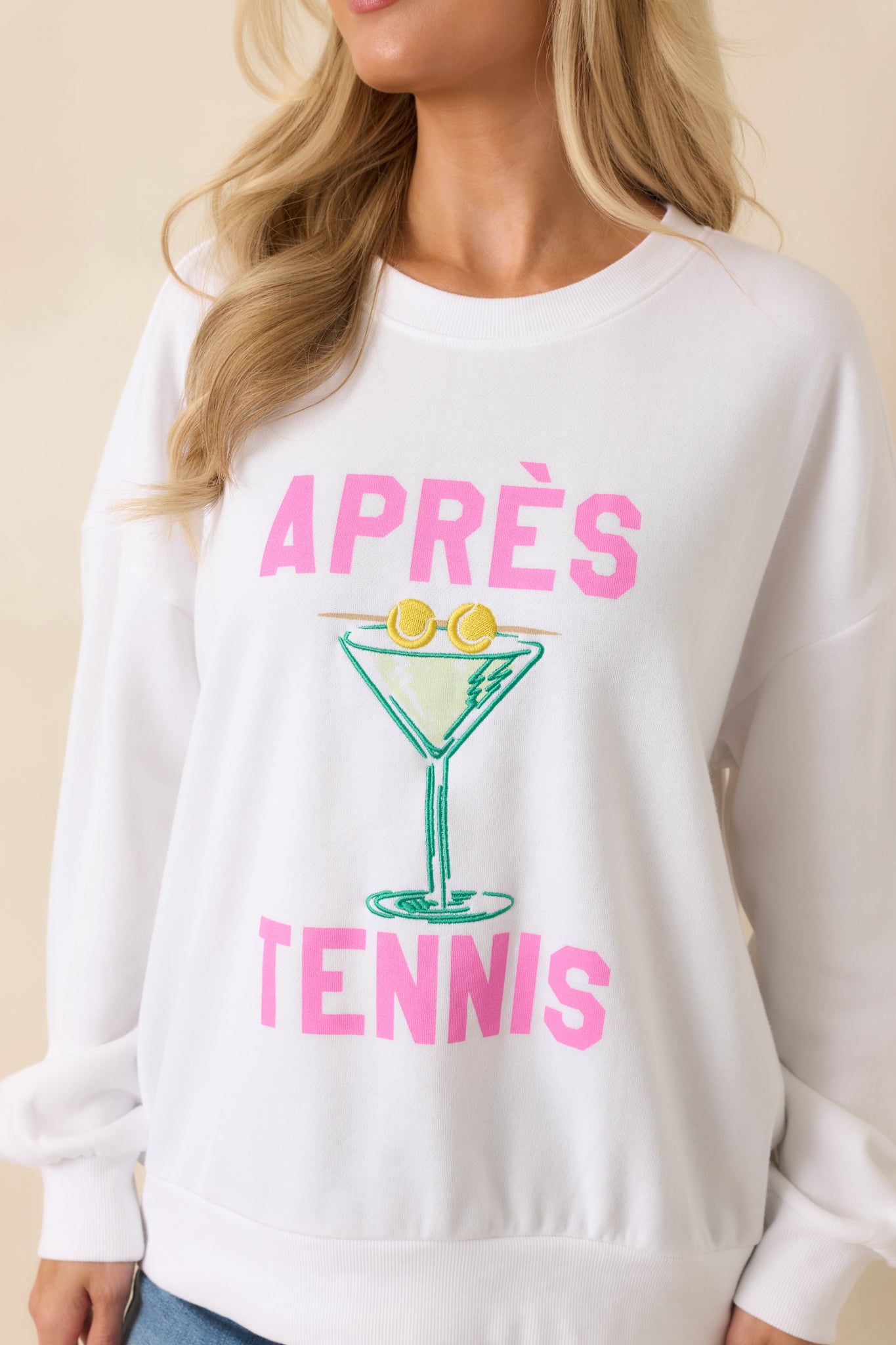 Close-up of the embroidered martini glass graphic, tennis ball accents, and raised pink "APRÈS TENNIS" lettering on the soft fleece fabric.
