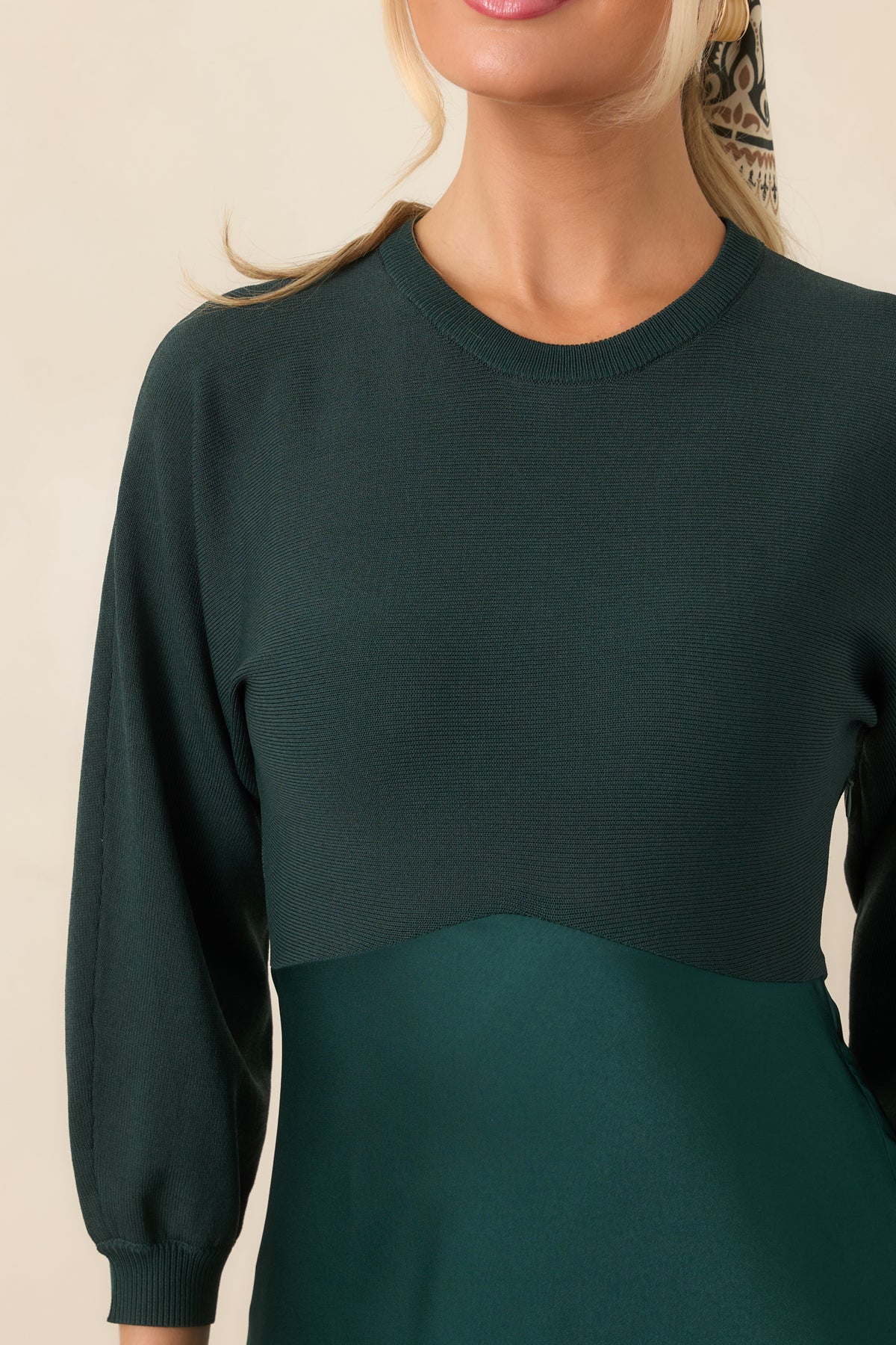 Close-up of the emerald knit bodice showing its round neckline, three-quarter sleeve, and transition into the satin skirt.