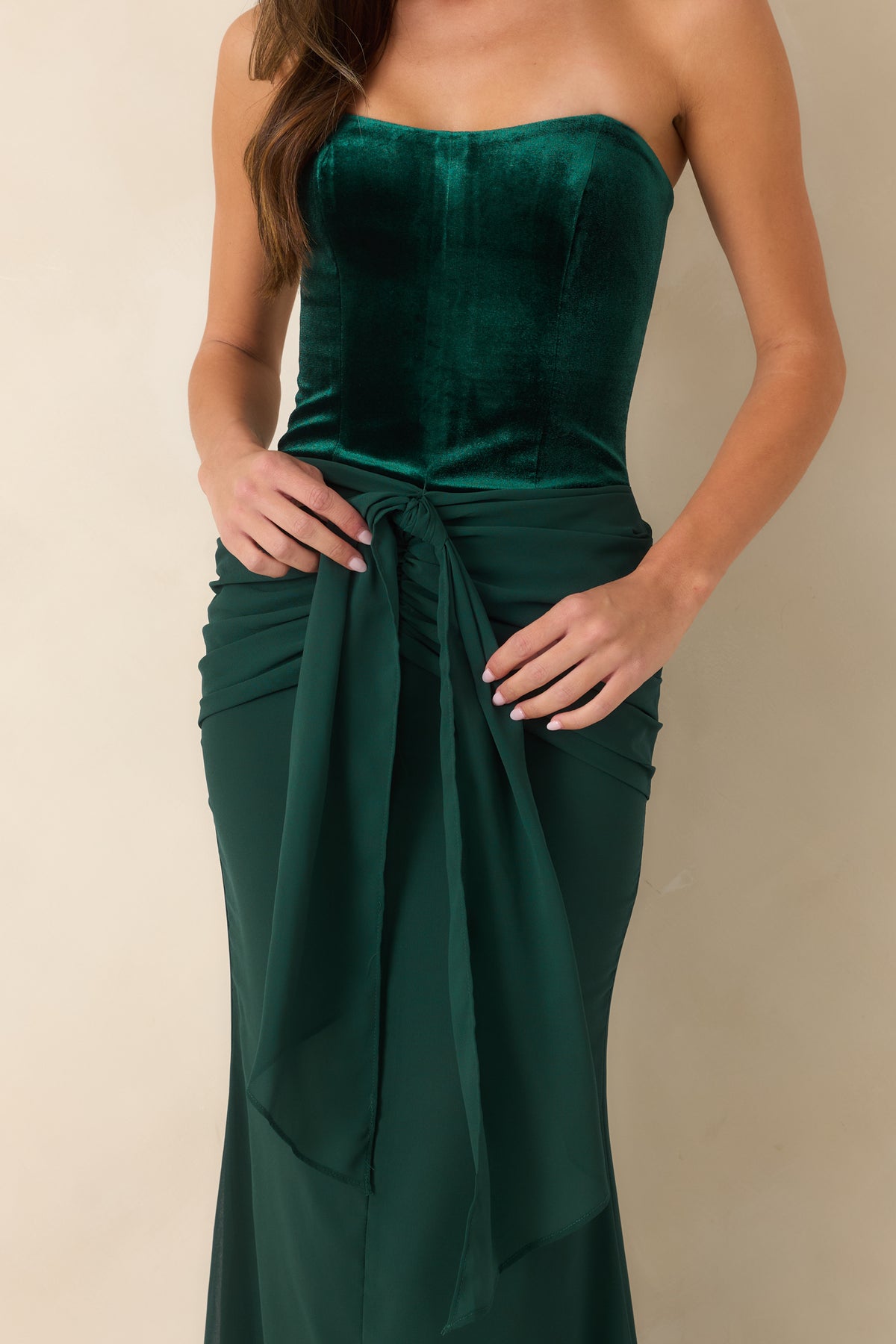 Rich emerald velvet dress showcasing the structured bodice, ruched hips, and draped front tie detail.