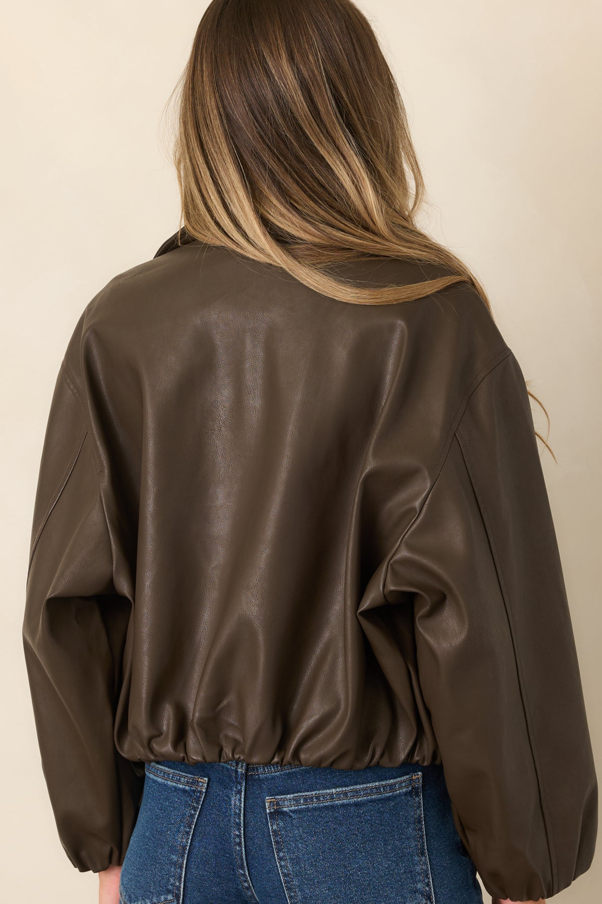 Rear of the espresso faux leather jacket showing the dropped shoulders, voluminous balloon sleeves, and gathered hem.
