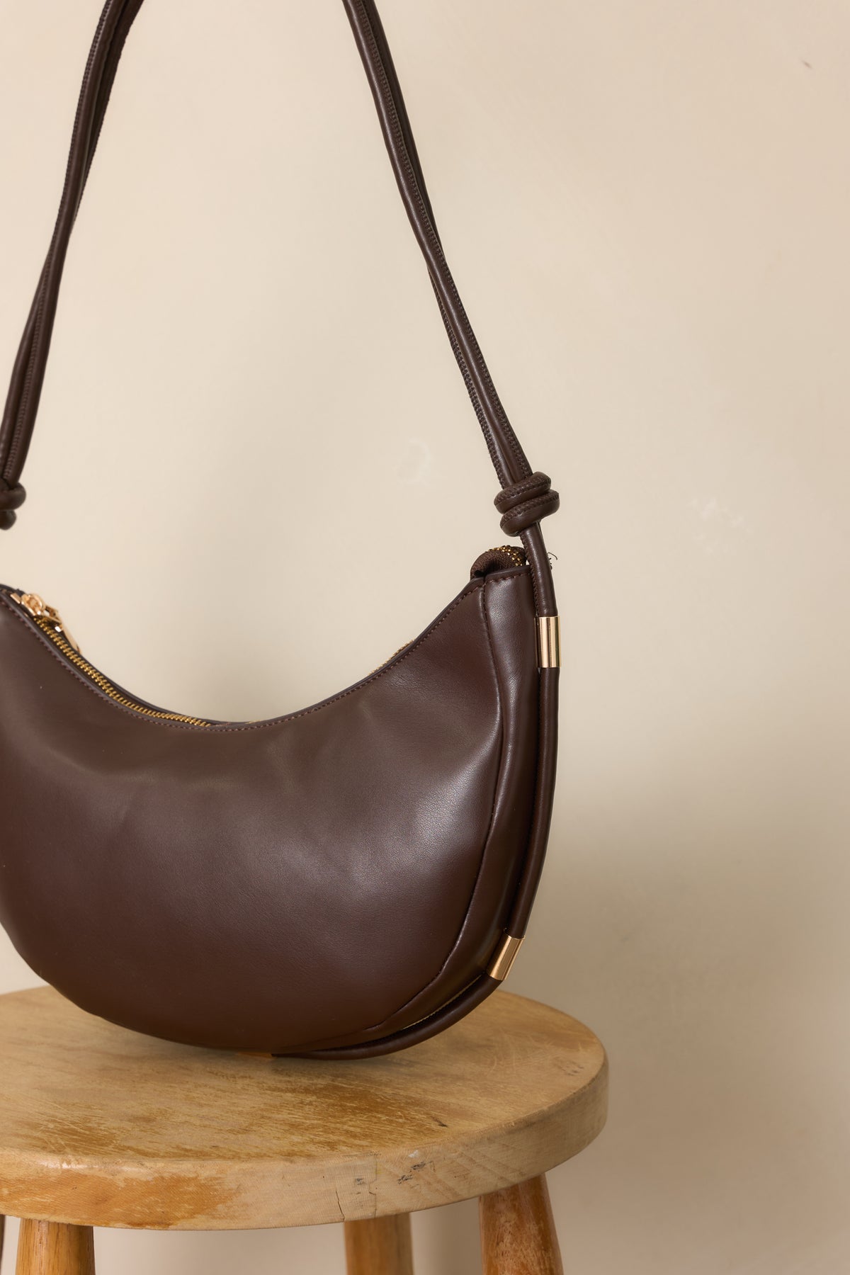 Close-up of the espresso handbag revealing the knotted strap detailing, polished gold-tone accents, and rich finish.