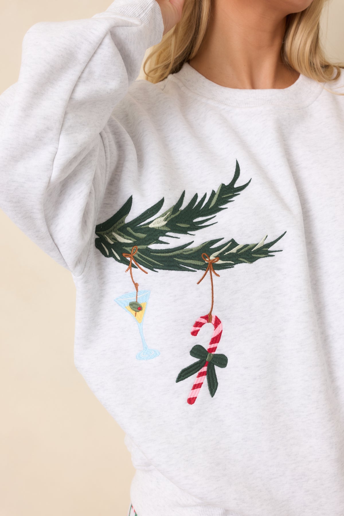 Close-up of embroidered evergreen branches decorated with a colorful cocktail glass, candy cane, and reindeer ornaments.