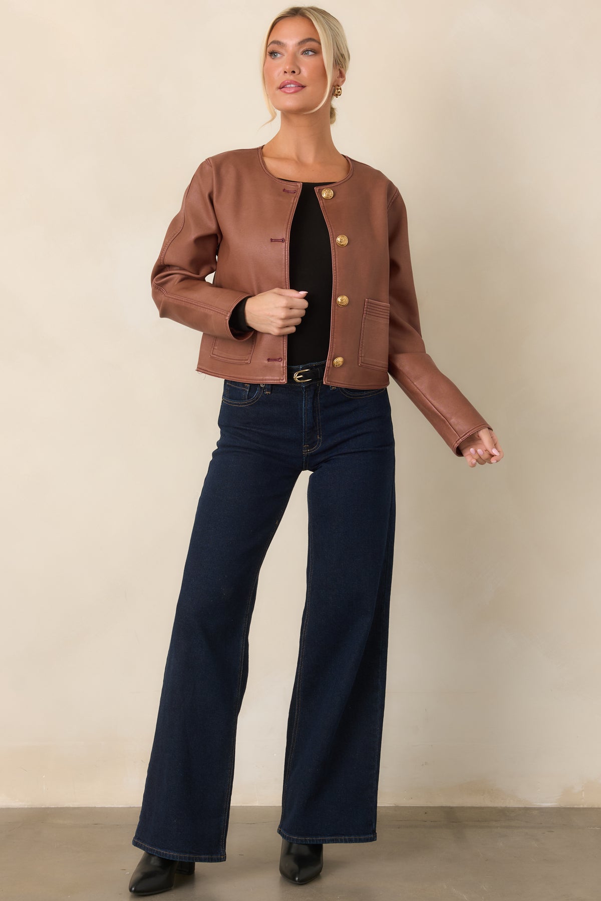 Faux leather jacket showcasing a sleek cropped silhouette, round neckline, and embossed gold buttons.