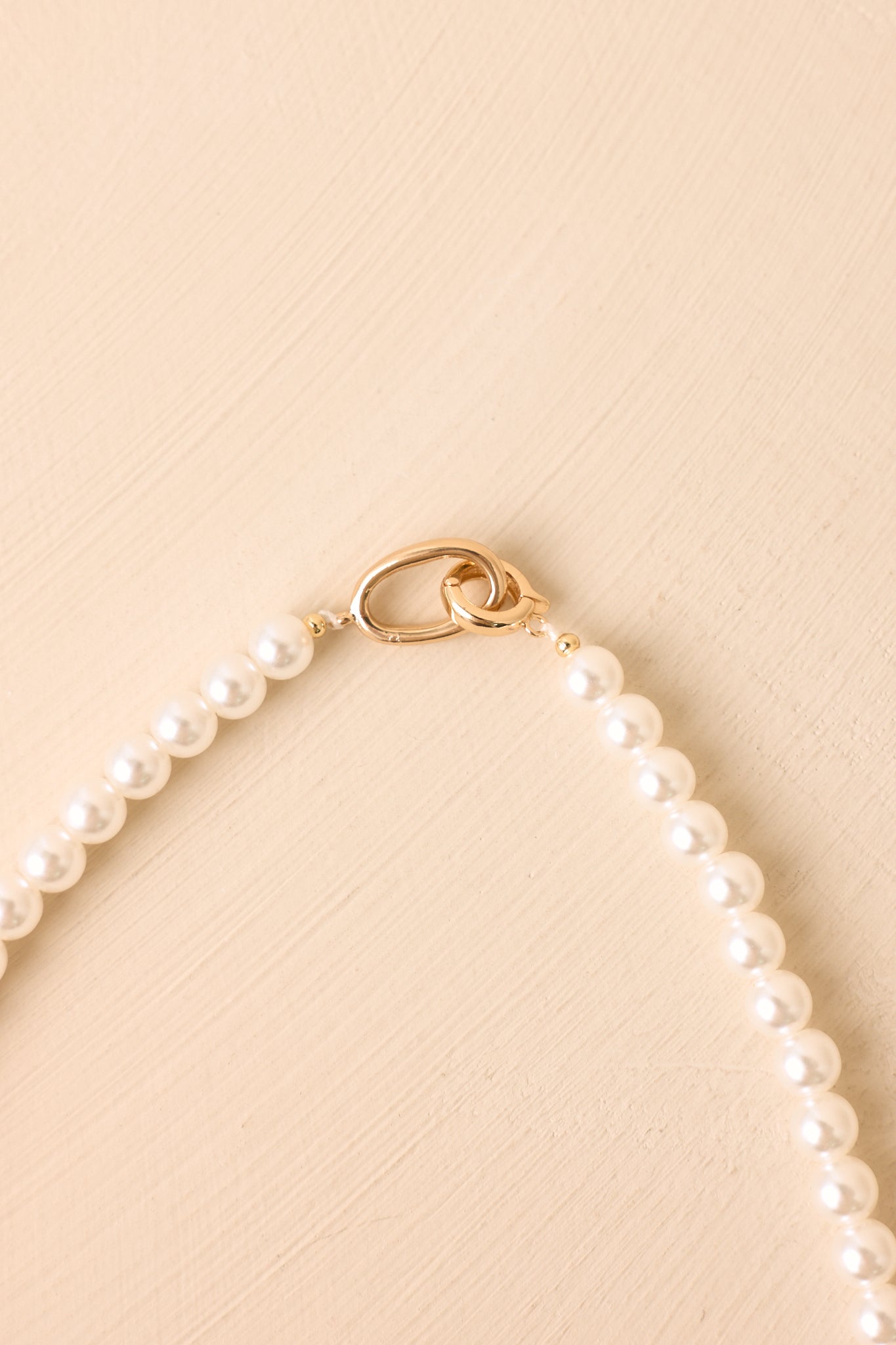Polished to Perfection faux pearl necklace displayed against a beige background to highlight the luminous pearls and polished gold-tone clasp.