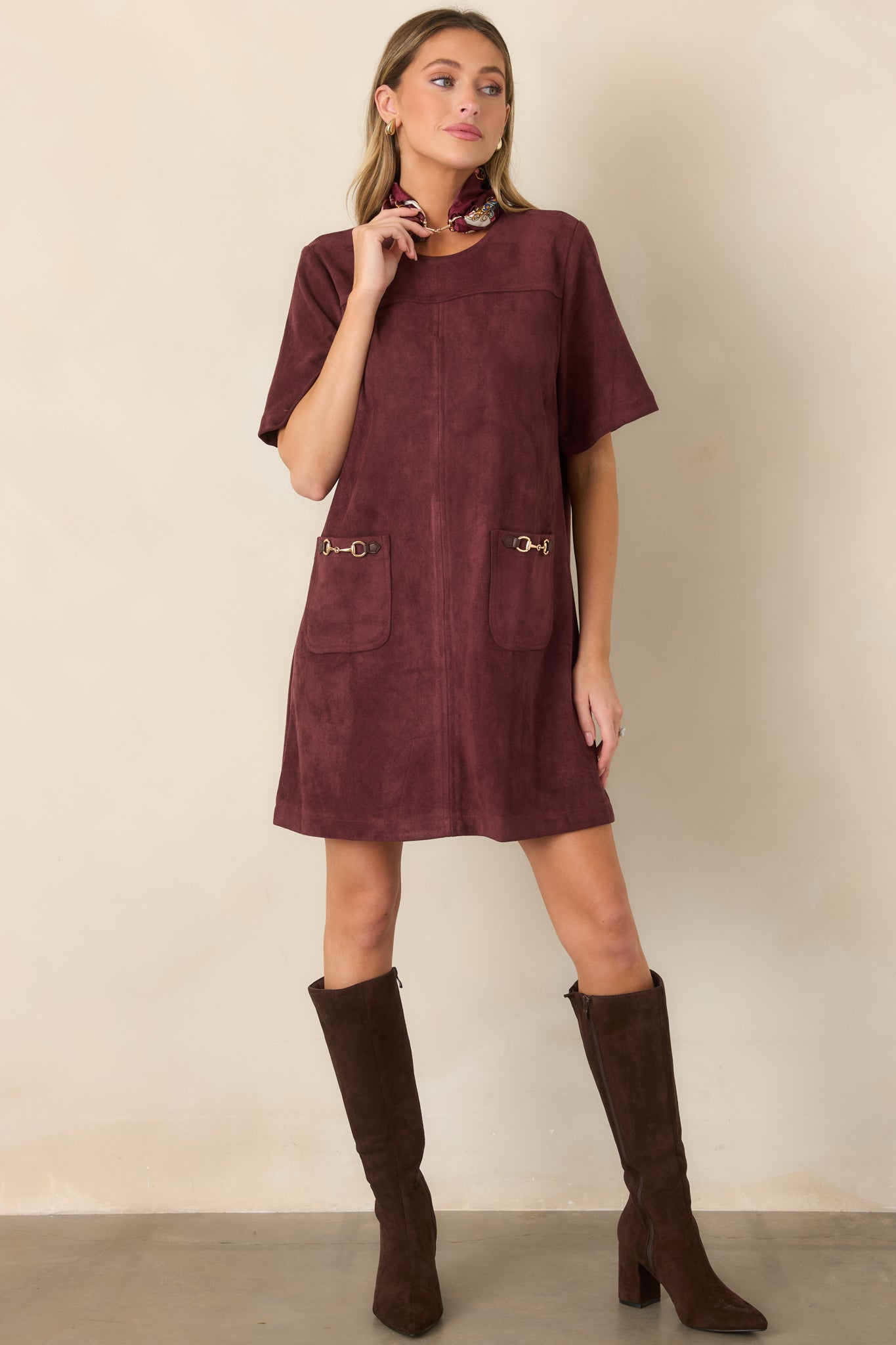 Stretch faux suede mini dress featuring a round neckline, short sleeves, front patch pockets, and gold-tone horsebit accents for an equestrian-inspired finish.