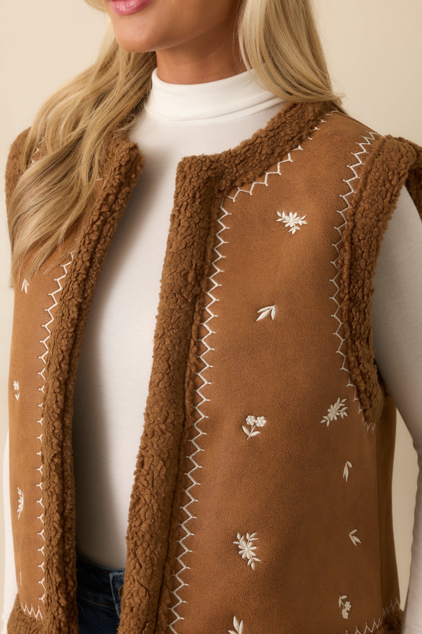 Close-up of the faux suede fabric, ivory floral embroidery, and soft faux shearling trim along the neckline.