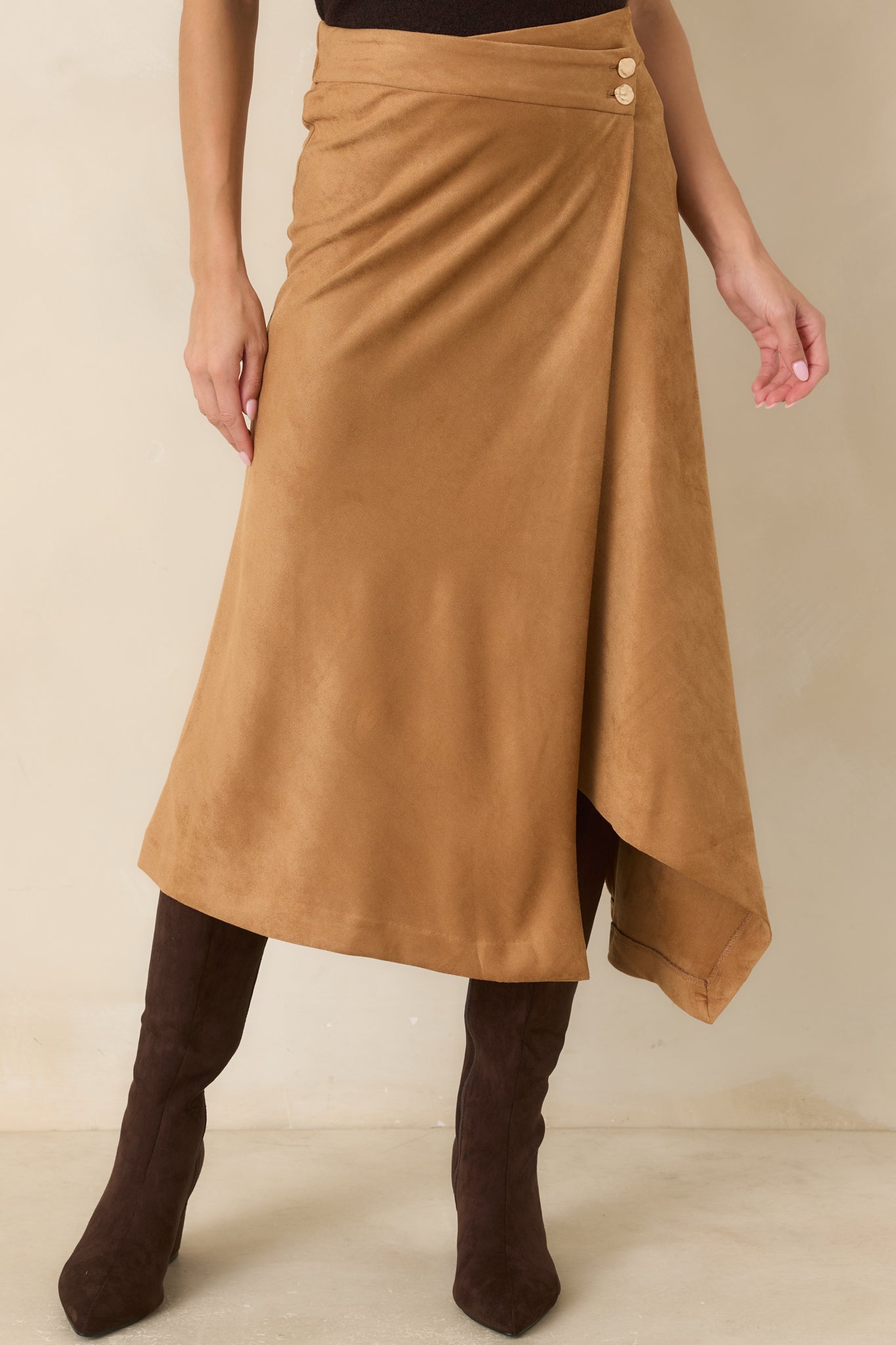 Close view of the faux suede skirt highlighting the asymmetrical wrap front, high-rise waistband, and hammered gold-tone button accents.
