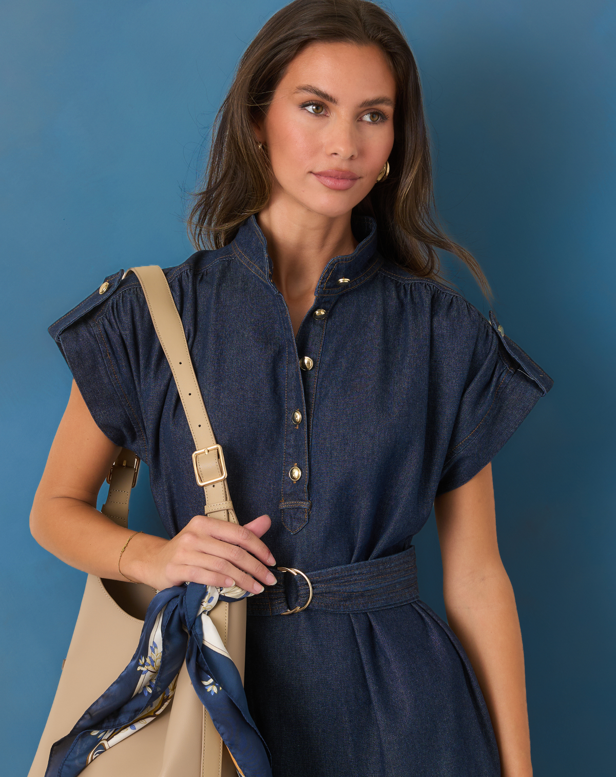 Model wearing denim dress and cream handbag.