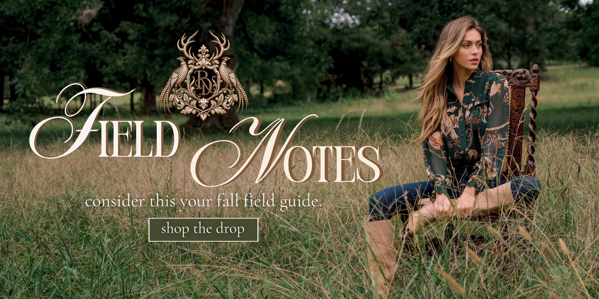 Girl sitting on a chair in a field wearing a green and brown top and boots with skinny jeans.