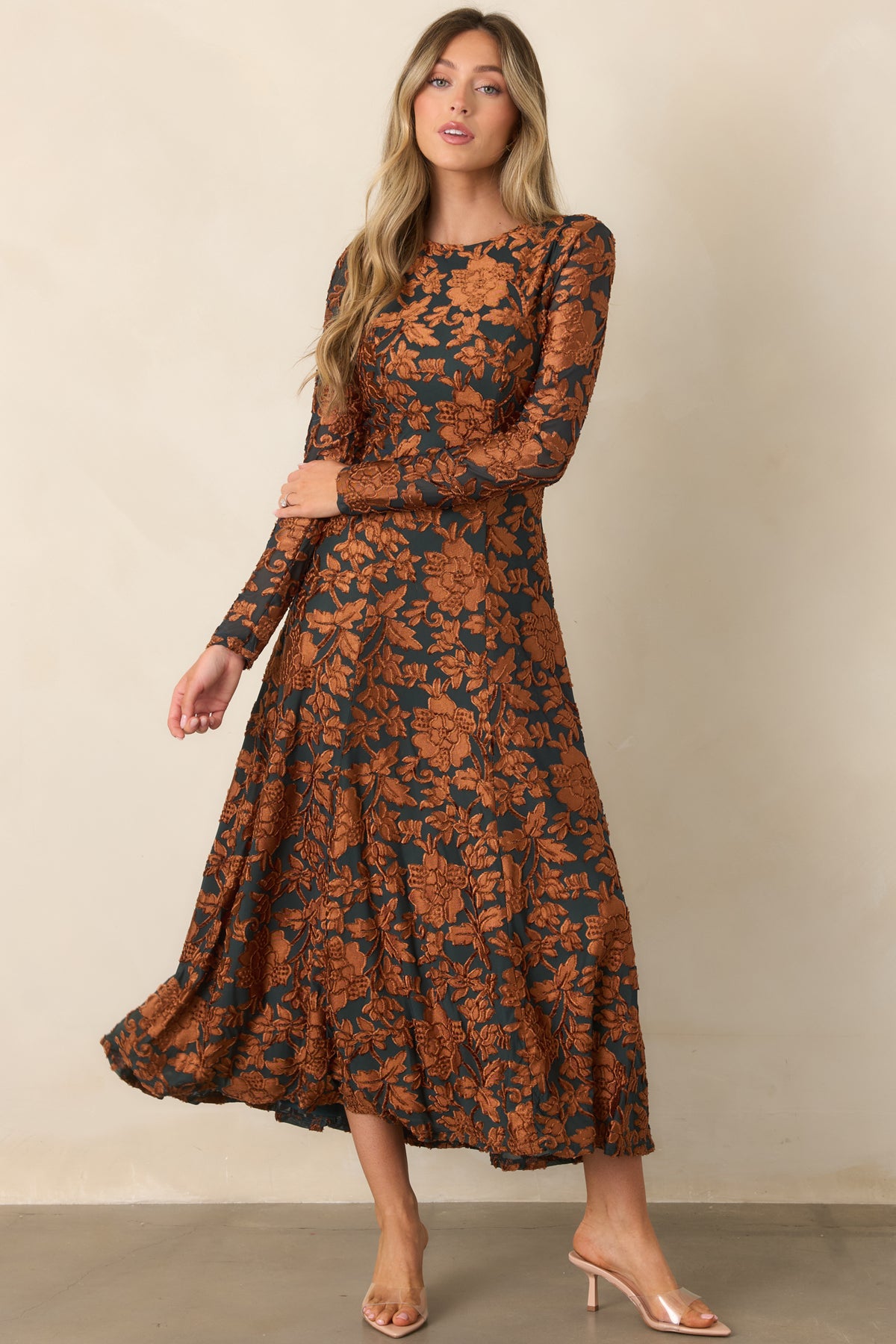 Fitted deep green dress with textured copper florals across the bodice, long sleeves, and a softly flowing skirt.