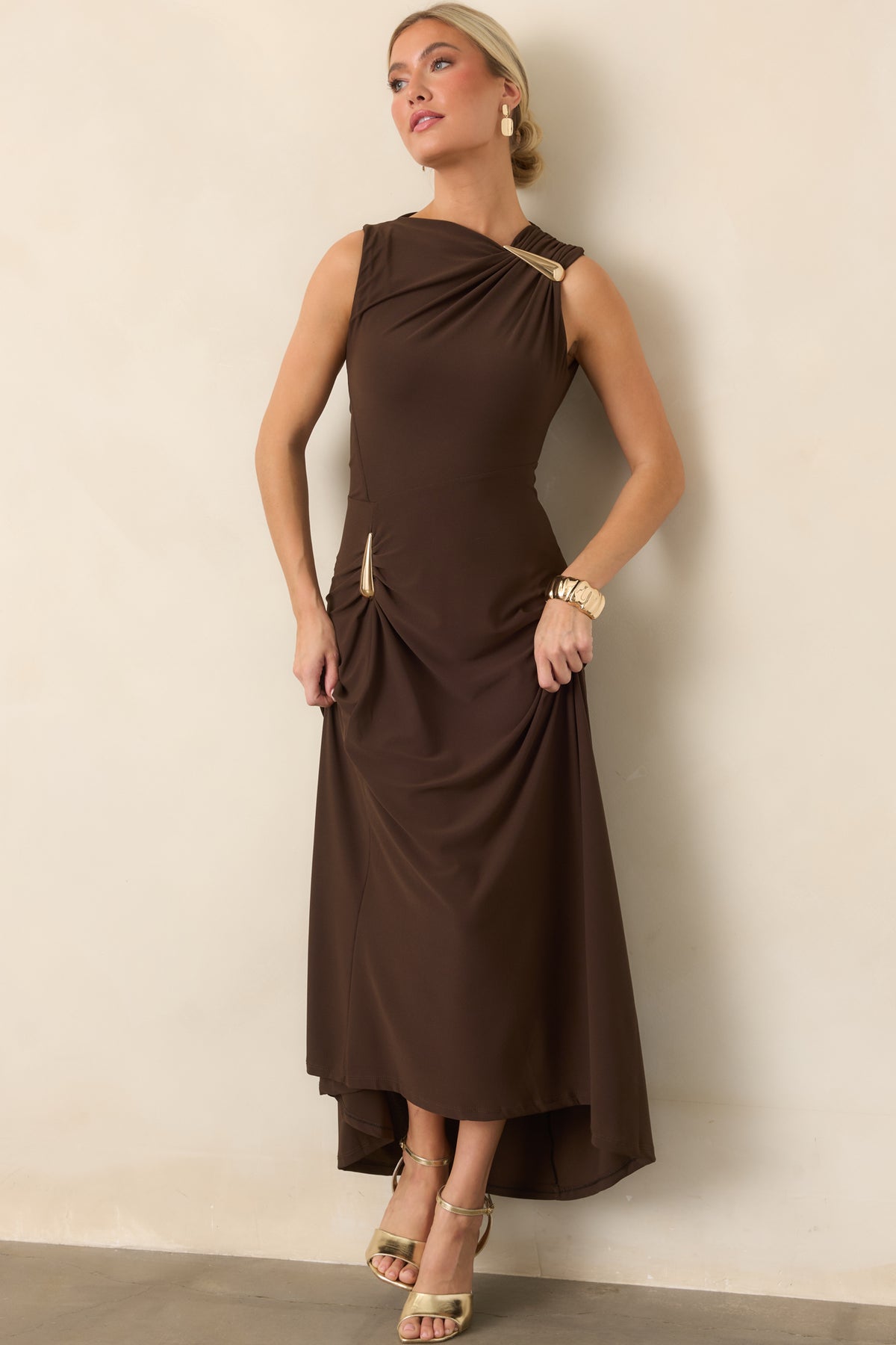 Fitted maxi dress highlighting the draped neckline, sculptural gold-tone accent, and gently flared silhouette.