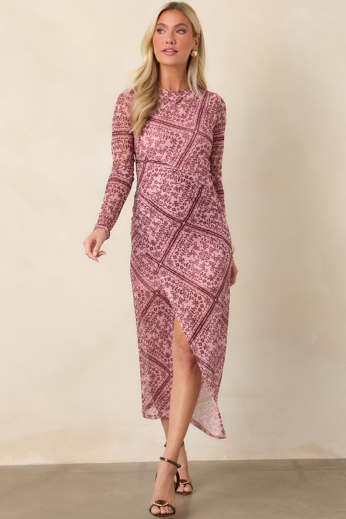 Fitted stretch dress featuring a softly ruched waist, sheer long sleeves, round neckline, and a flowing front skirt slit.