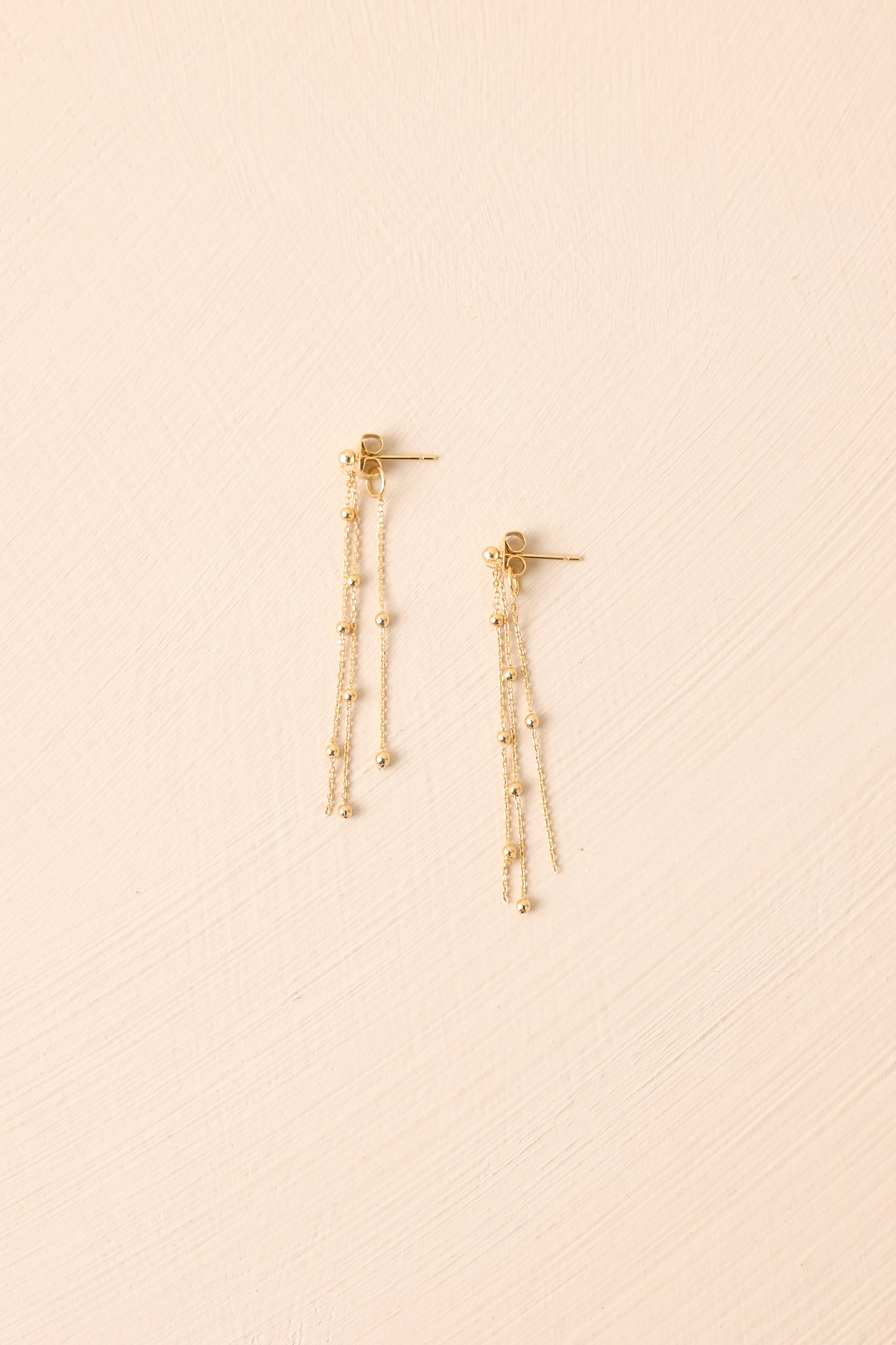 Flat lay of the earrings on a beige surface emphasizing the polished finish, fine cable chains, and smaller bead details.