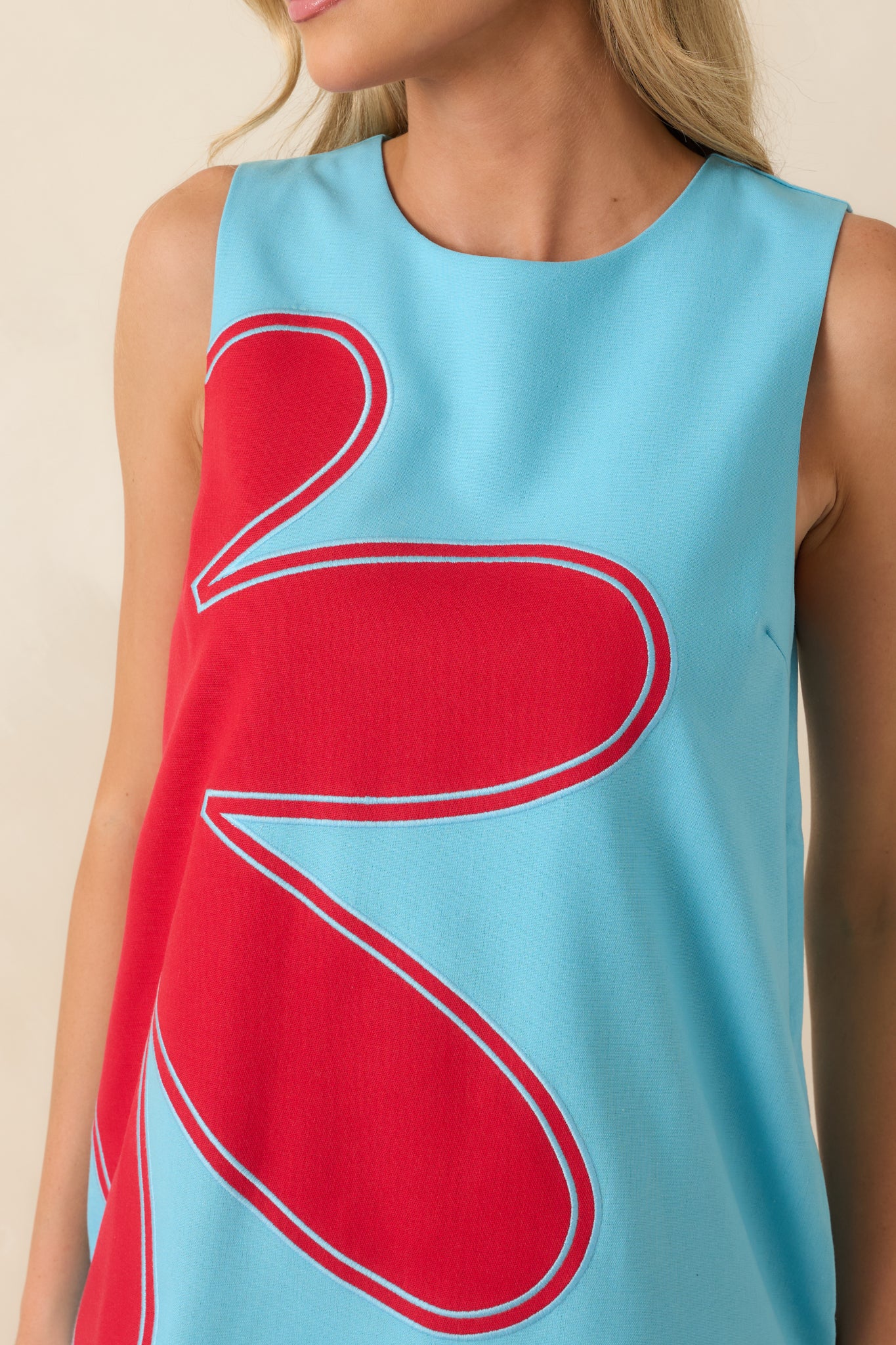 Detailed view of the oversized red floral appliqué, embroidered outlines, and textured linen blend fabric.