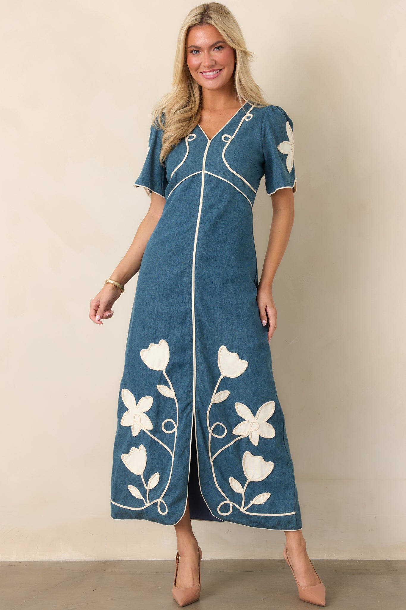 Flared maxi dress featuring a flattering V-neckline, short sleeves, defined waist, ivory floral appliqué, and coordinating piping.