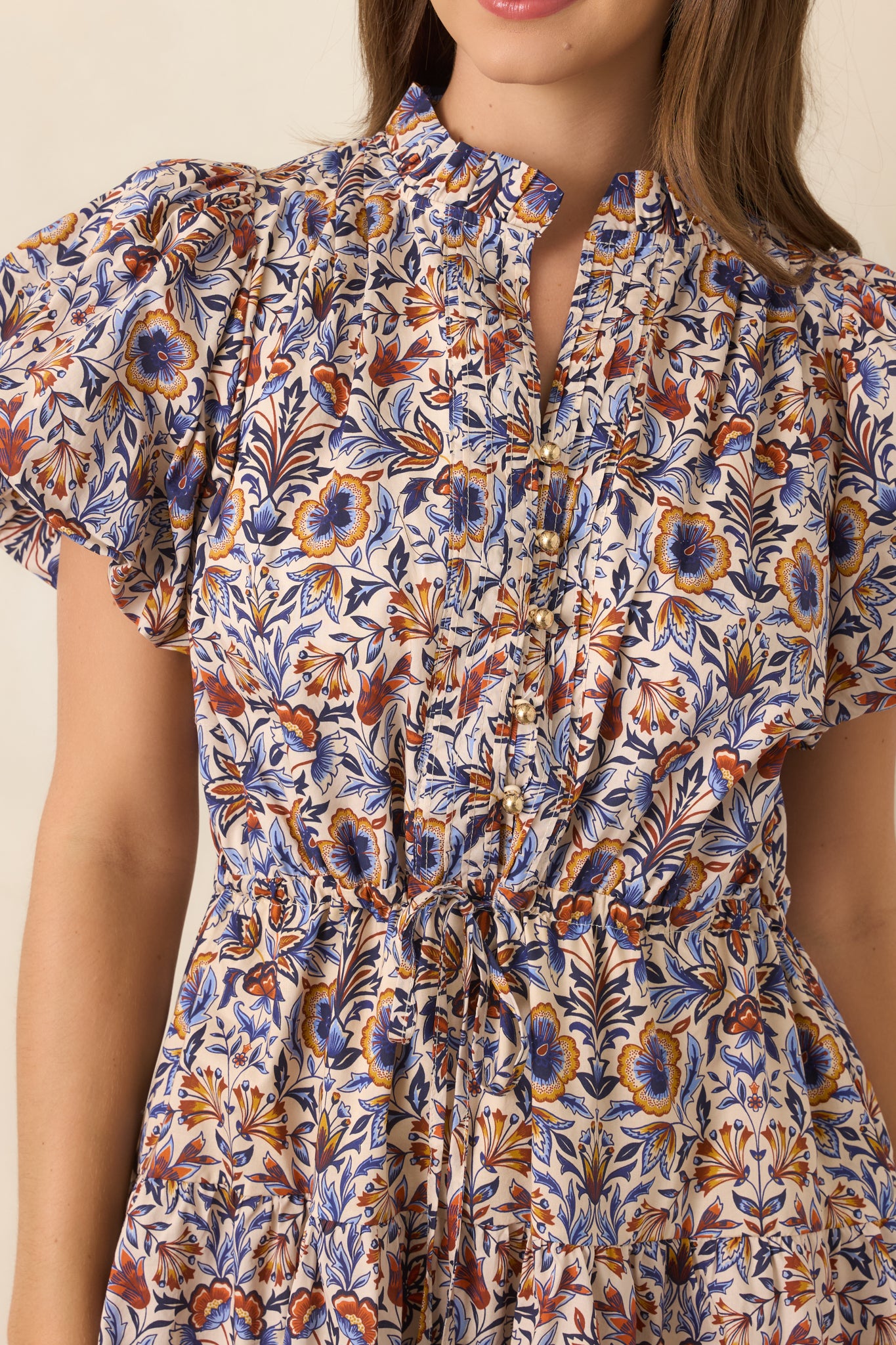 Close-up of the pleated neckline area with gold-tone buttons and colorful floral detailing.