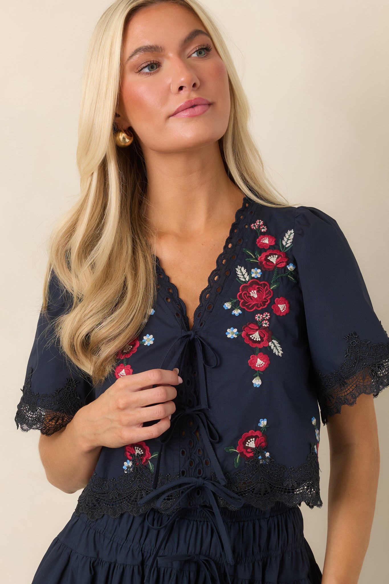 Detailed view of the embroidered cotton top highlighting its colorful floral pattern, V-neckline, and three tie-front closures.