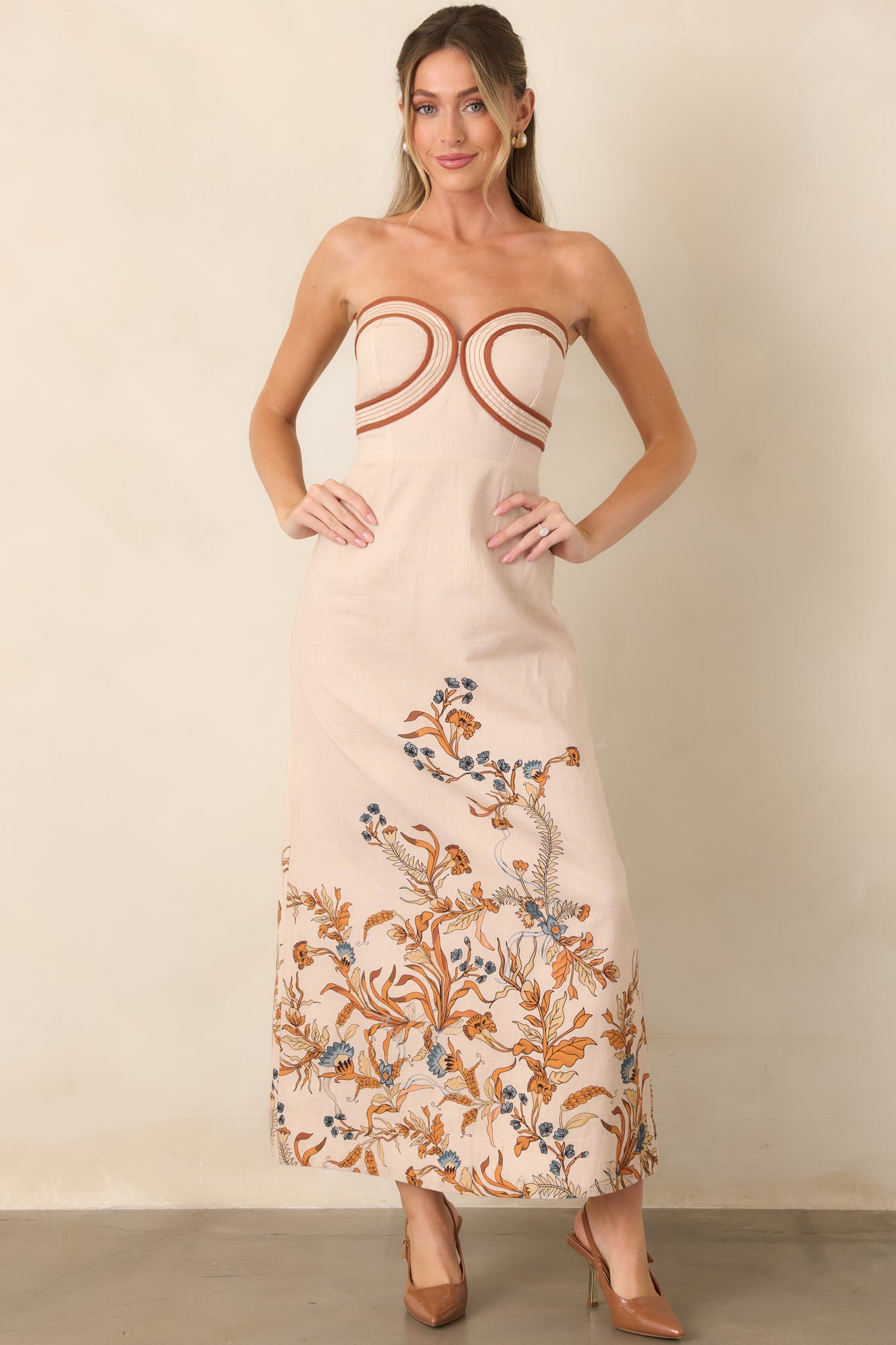 Strapless column dress featuring a structured bodice, defined waist, and burnt orange and muted blue floral accents along the lower skirt.